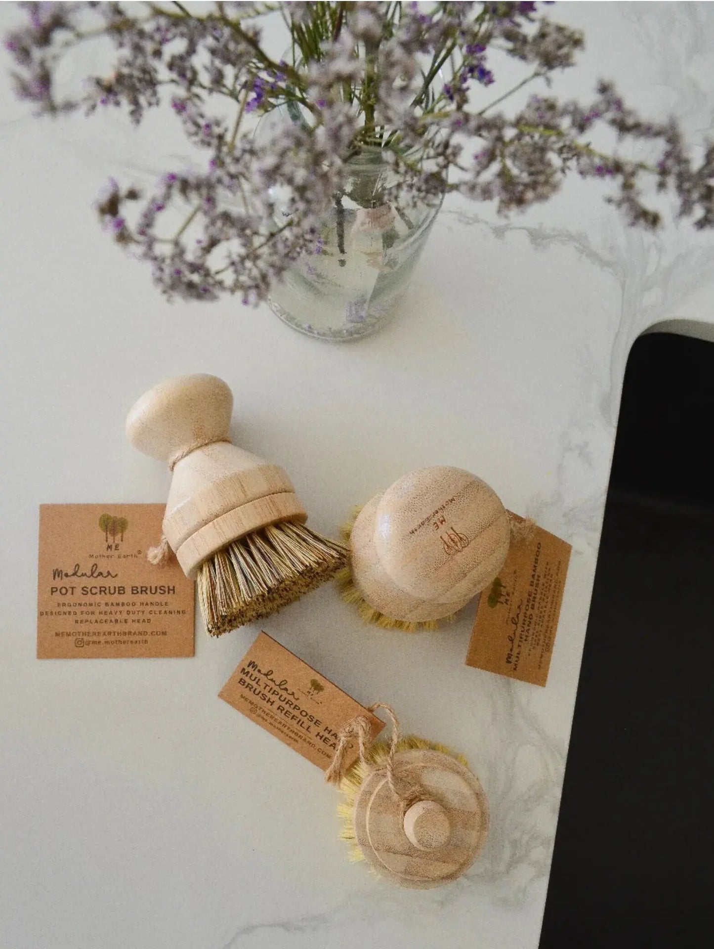 Set of wooden cleaning brushes with tags on a marble surface with flowers in the background