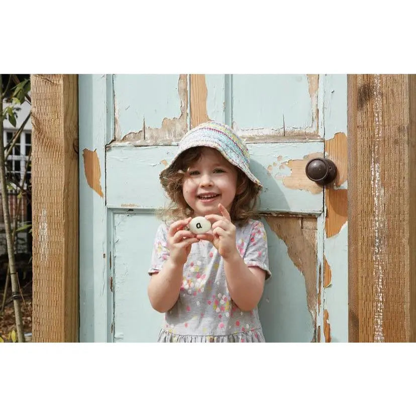A child holding an alphabet pebble in front of a mint green door