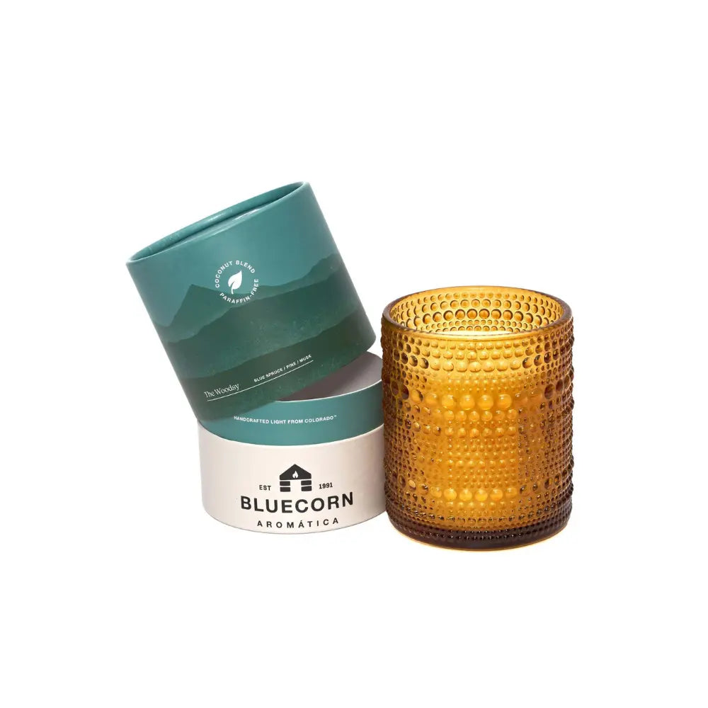 Orange textured candle next to Bluecorn Aromatica containers on a white background