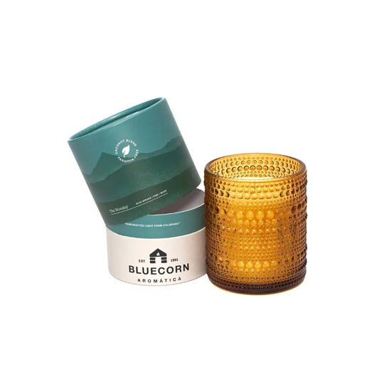 Orange textured candle next to Bluecorn Aromatica containers on a white background