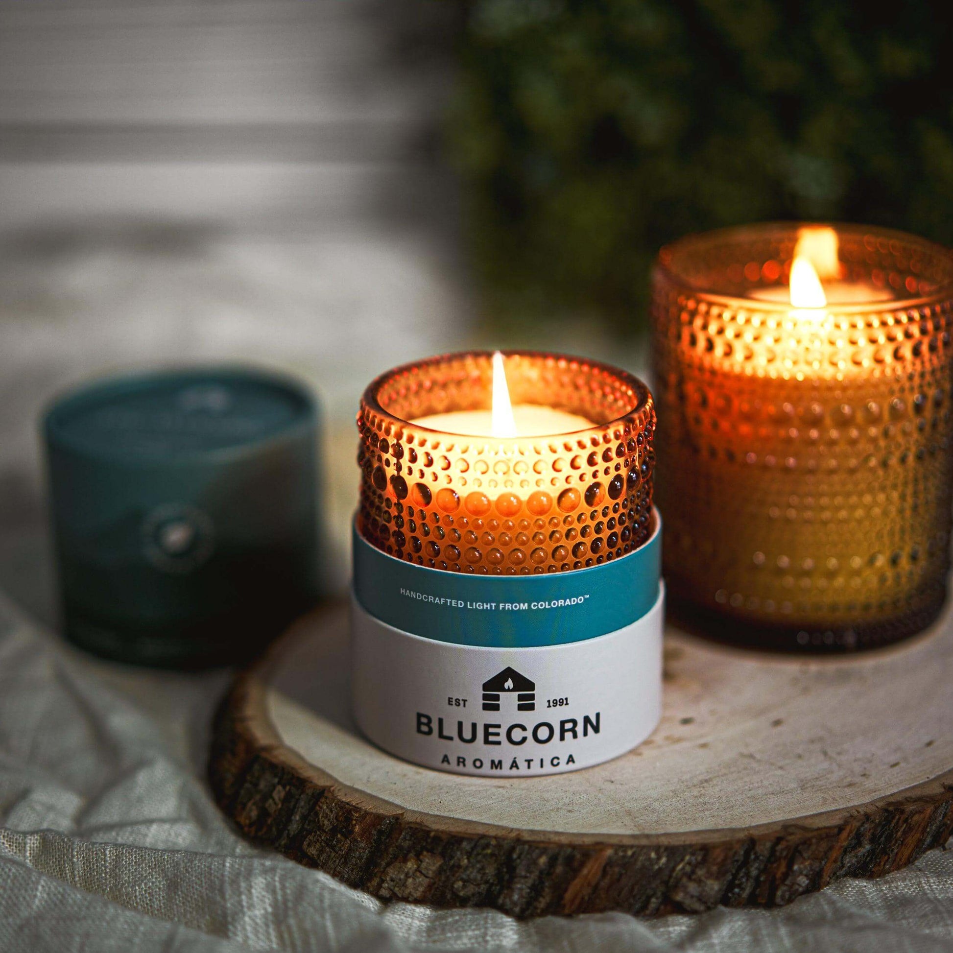 Bluecorn Aromática candle in a textured holder on a wooden surface with a blurred background