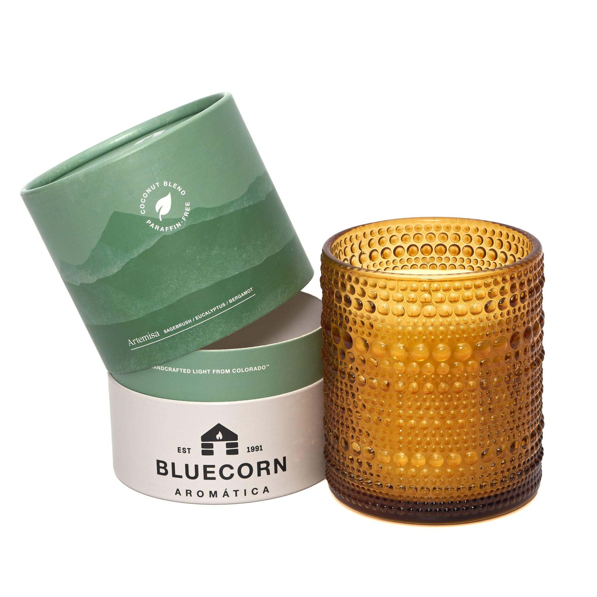 Amber glass candle with textured surface next to green and white packaging on a white background