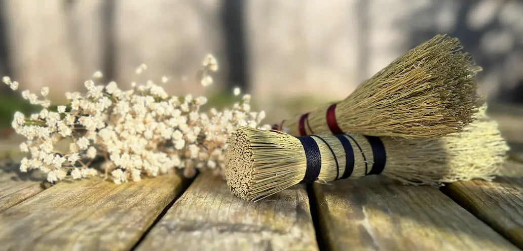 Two artisan brooms with decorative handles on a wooden surface