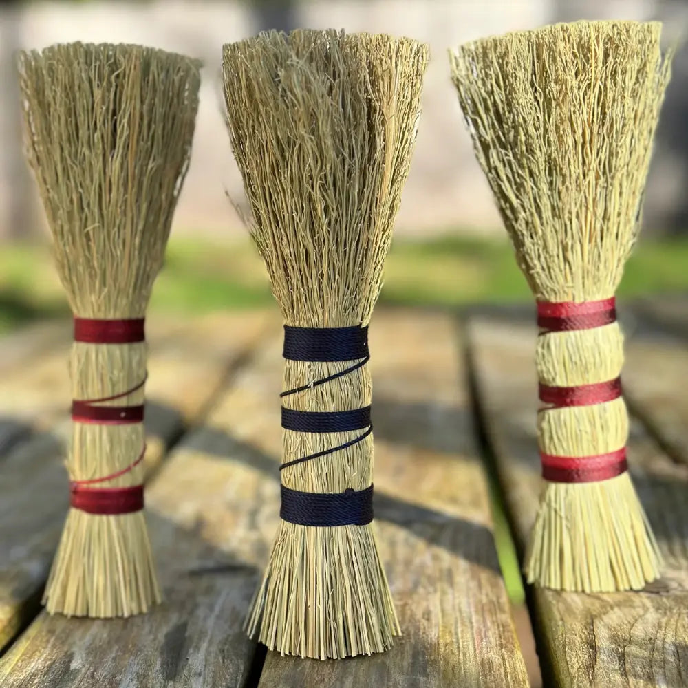 Three brooms with different colored bands on a wooden surface