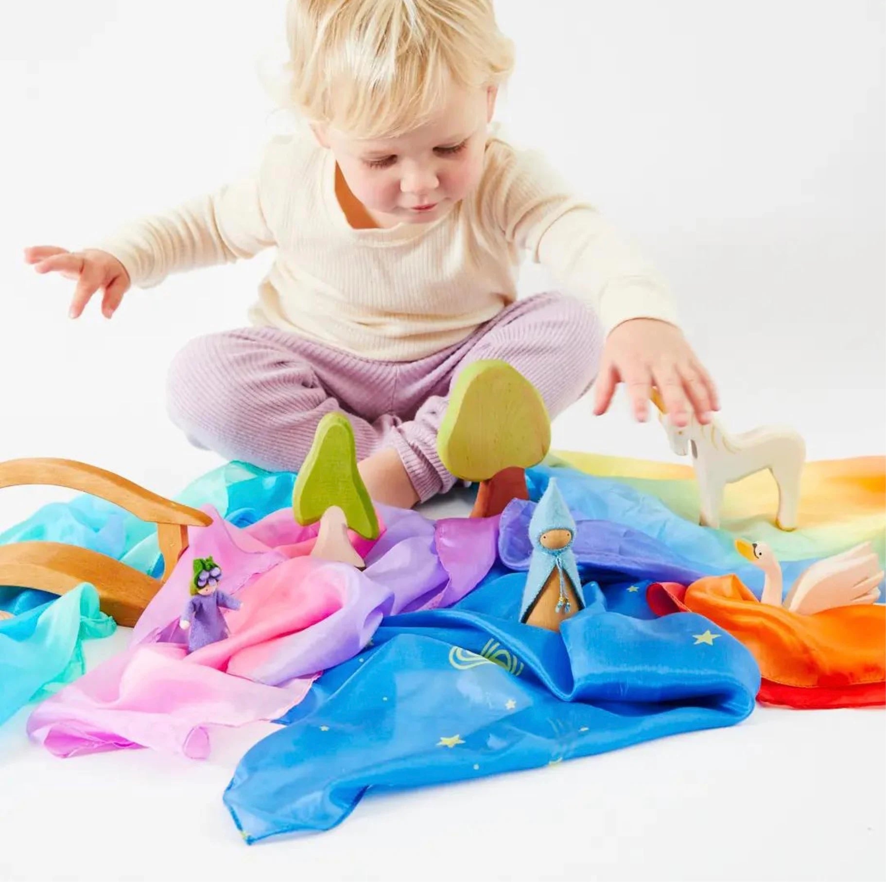 Toddler playing with assorted enchanted mini playsilks and wooden toys