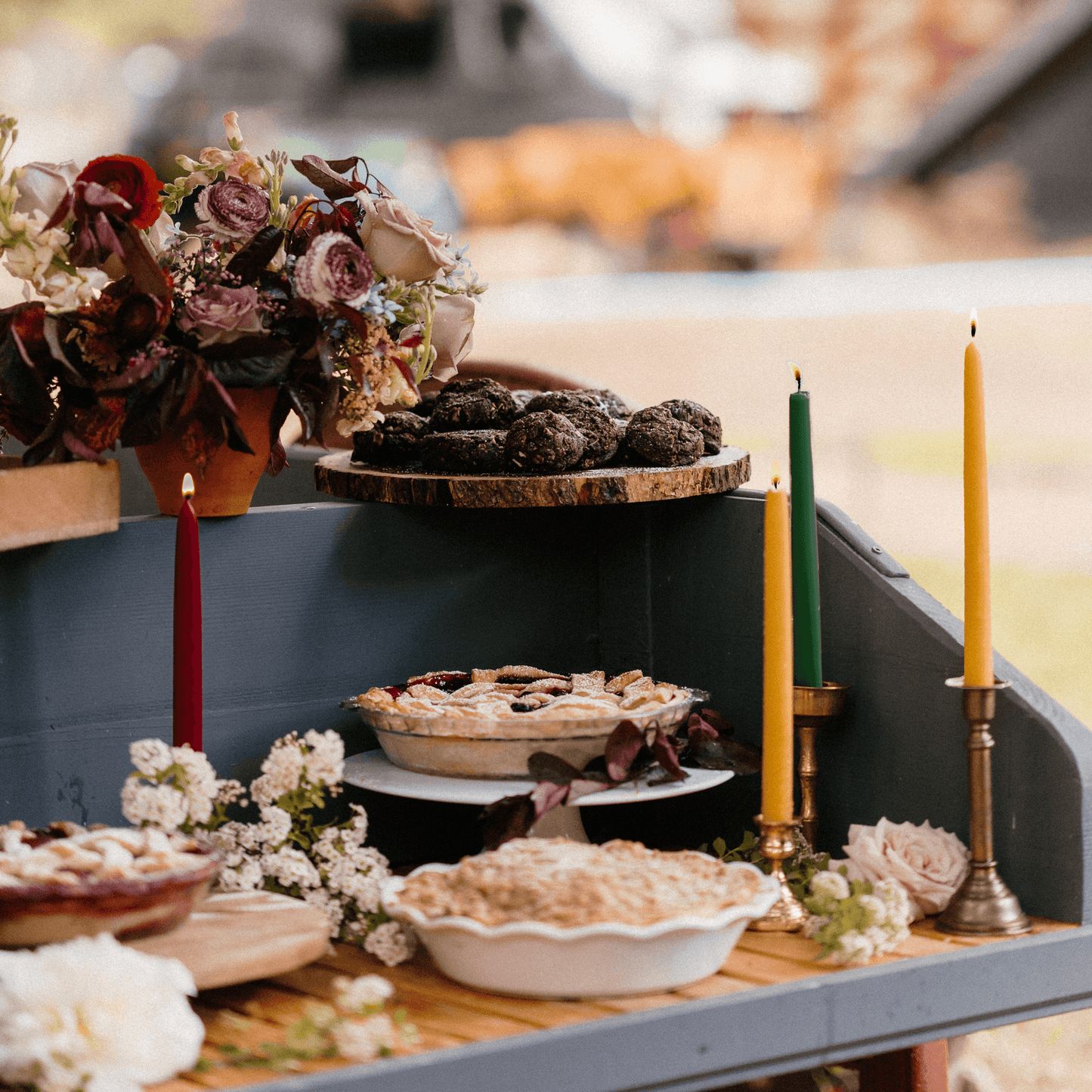 Display of pies and beeswax taper candles on a table with floral arrangements.