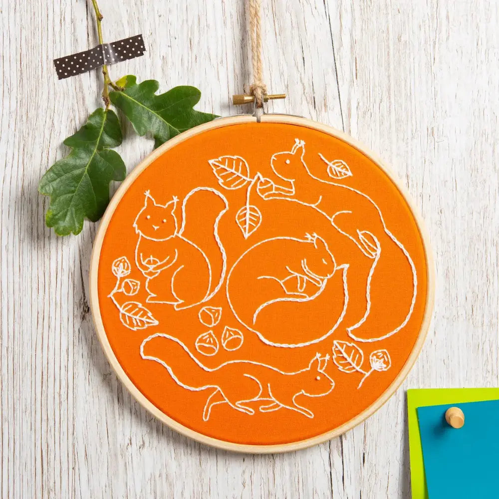 Autumn squirrel embroidery hoop with white stitched squirrels, leaves, and acorns on orange fabric