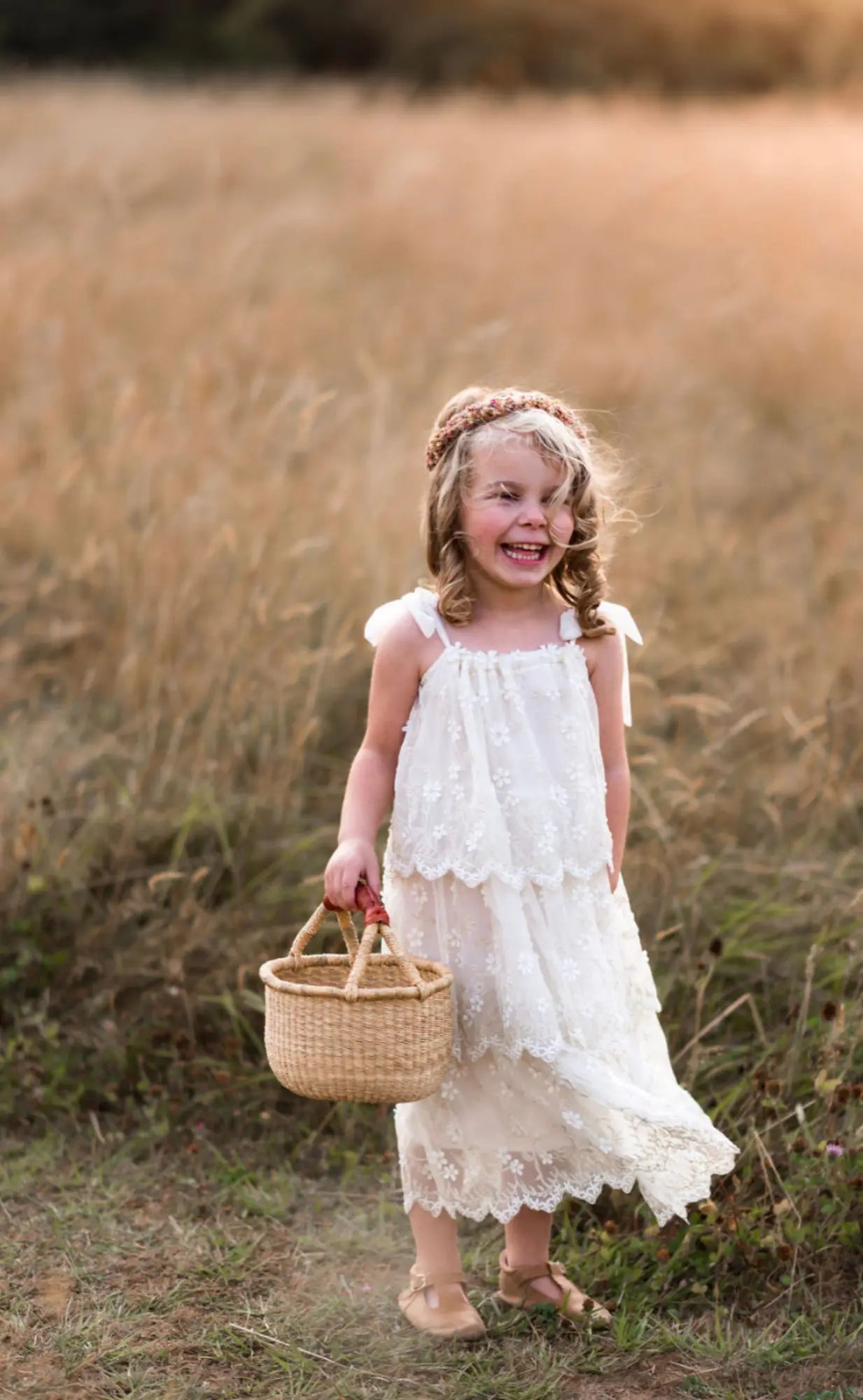 Young girl in a white dress holding a basket in a field