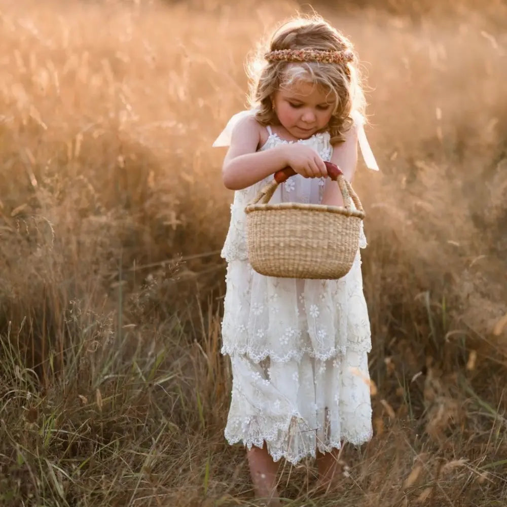 Young girl in a white dress holding a basket in a golden field