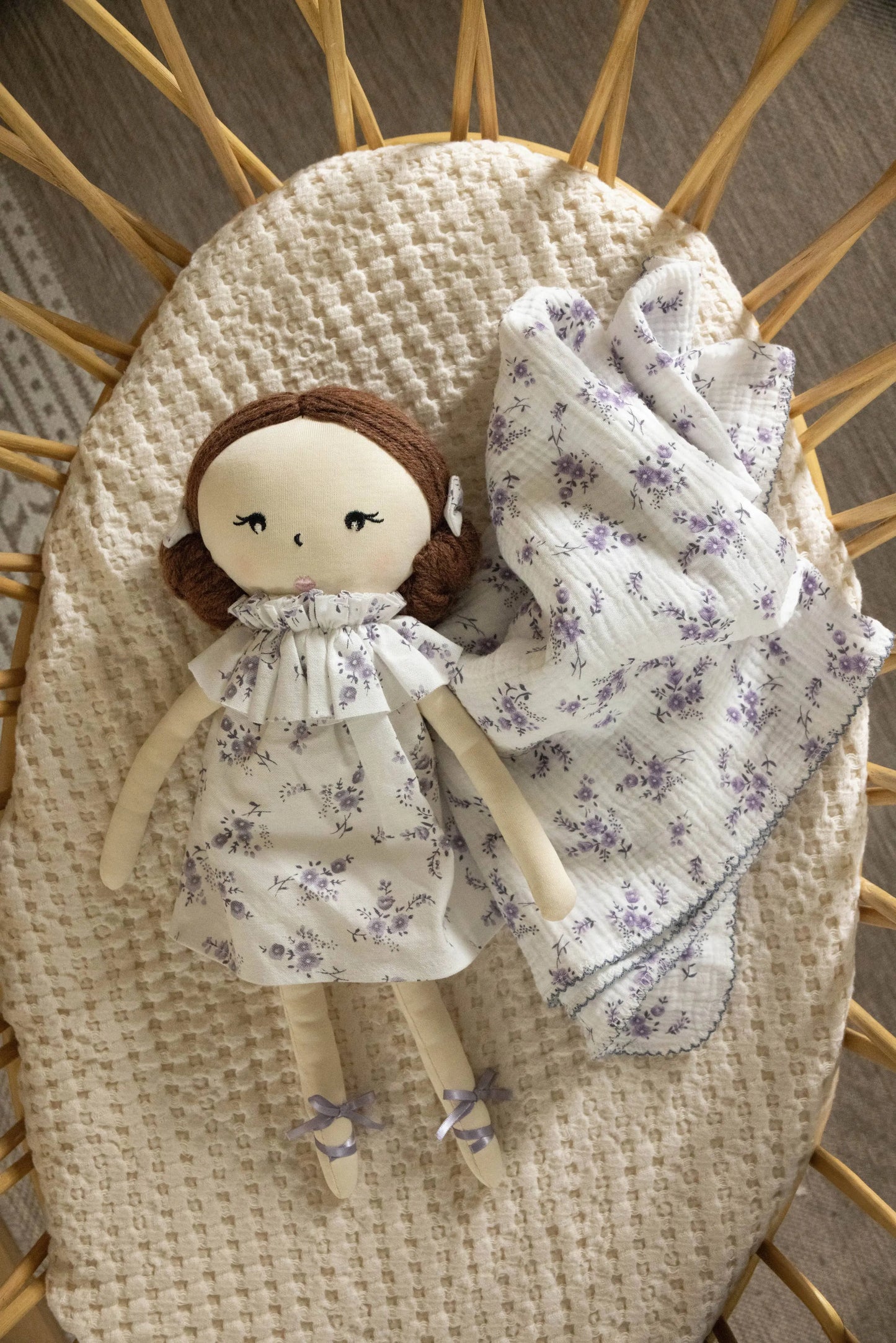 Doll with floral dress and blanket in a wicker basket