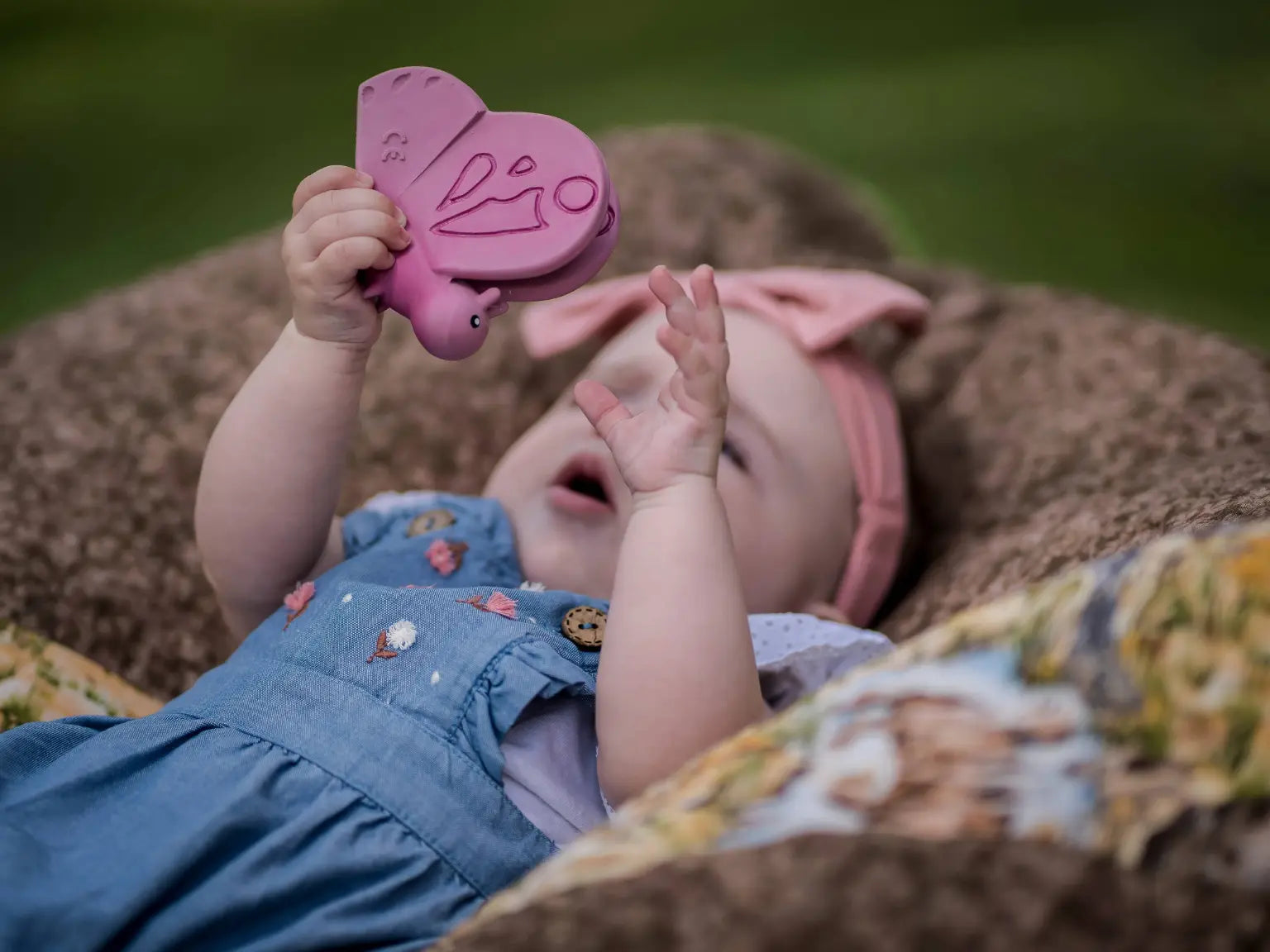 Infant lying on back holding natural rubber butterfly teether during sensory play