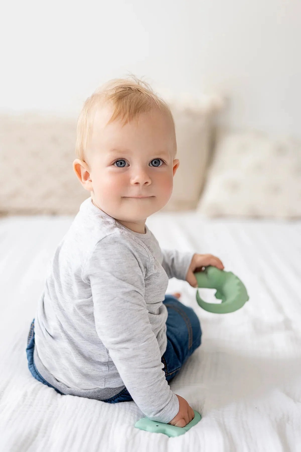 Baby holding natural rubber crocodile toy and looking over shoulder during sensory play