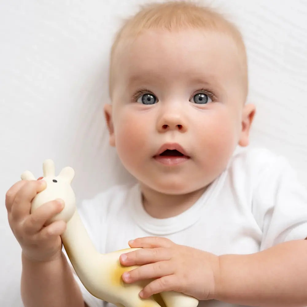 Baby holding natural rubber giraffe teether during sensory play