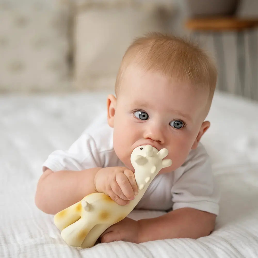 Baby lying on tummy holding and mouthing natural rubber giraffe teether during play