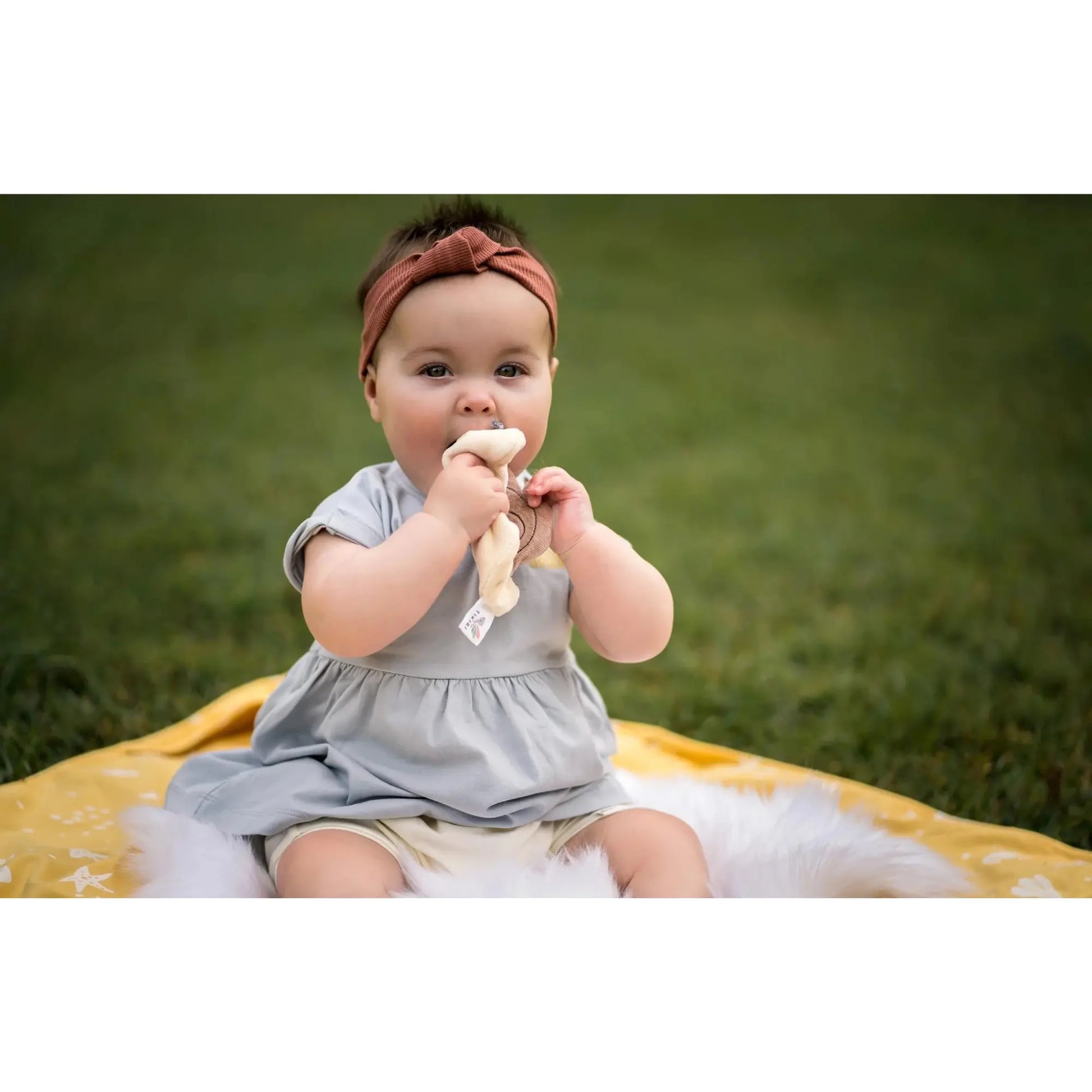 Infant sitting on blanket in grass playing with a snail sensory toy