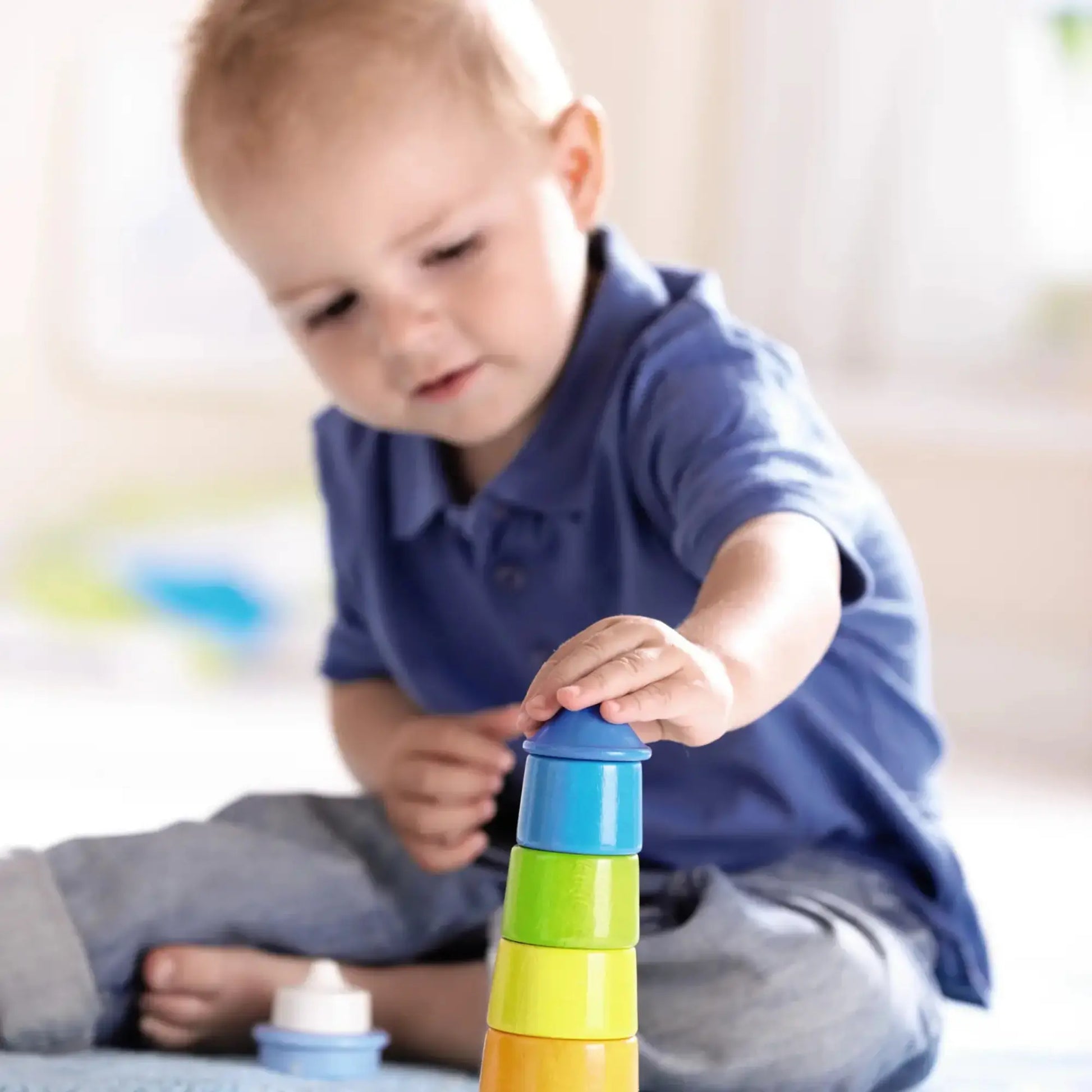 Baby playing with colorful wooden stacking toys on a light background