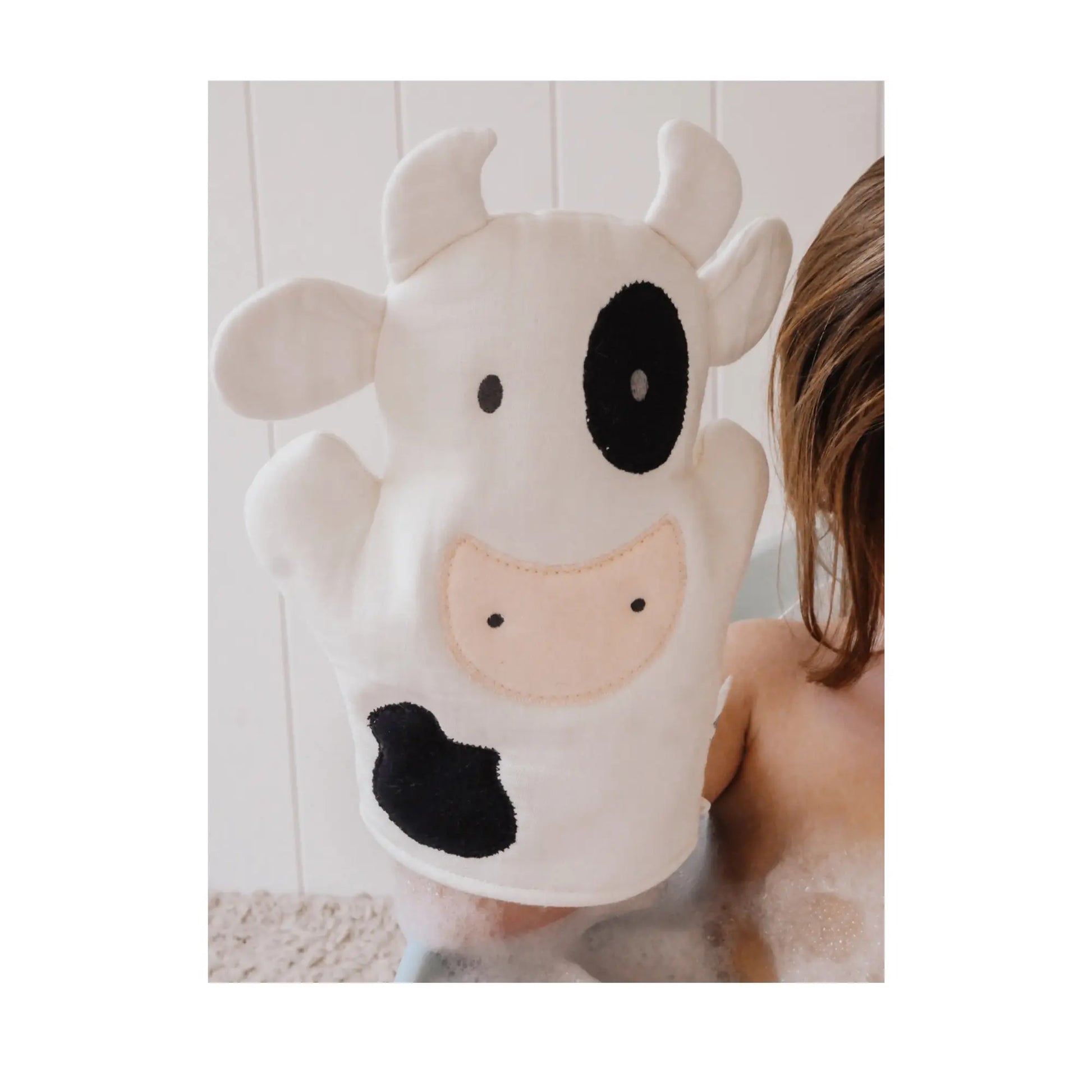 Toddler holding cow-shaped cotton muslin bath mitt in bubble bath