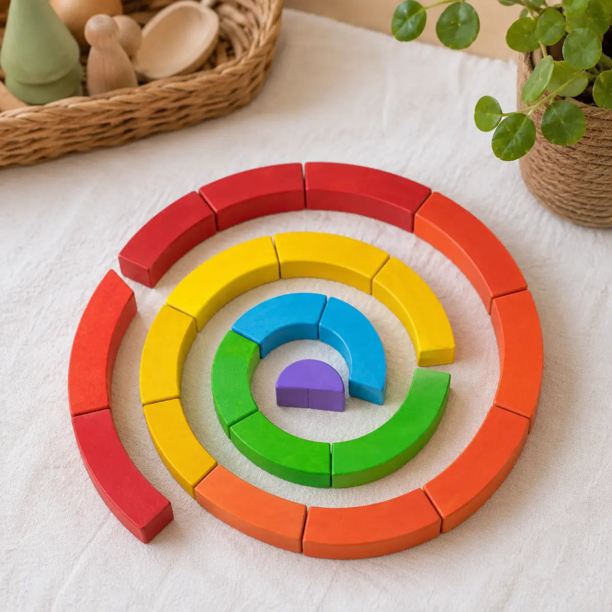 Colorful BAJO wooden curved blocks arranged in a spiral on a playroom cloth with natural toys nearby