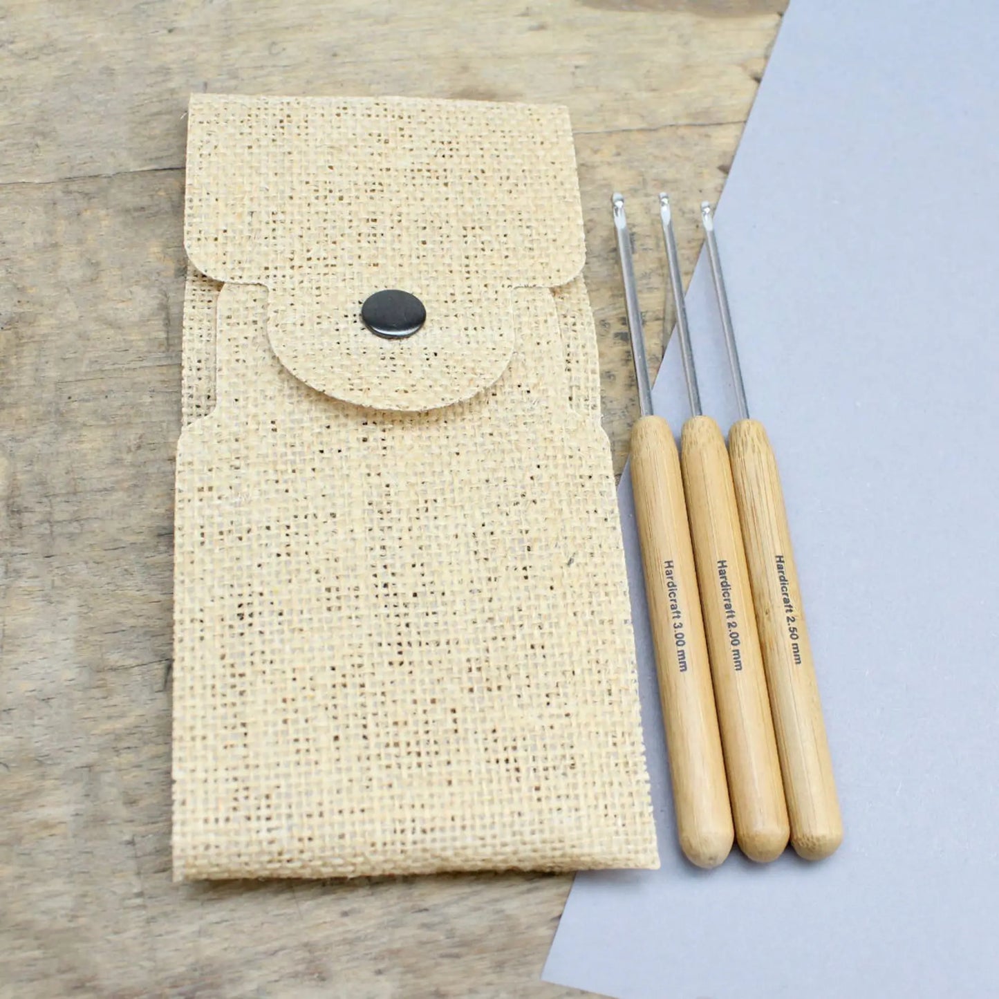 Three bamboo handle aluminum crochet hooks shown beside a natural burlap storage pouch on a tabletop