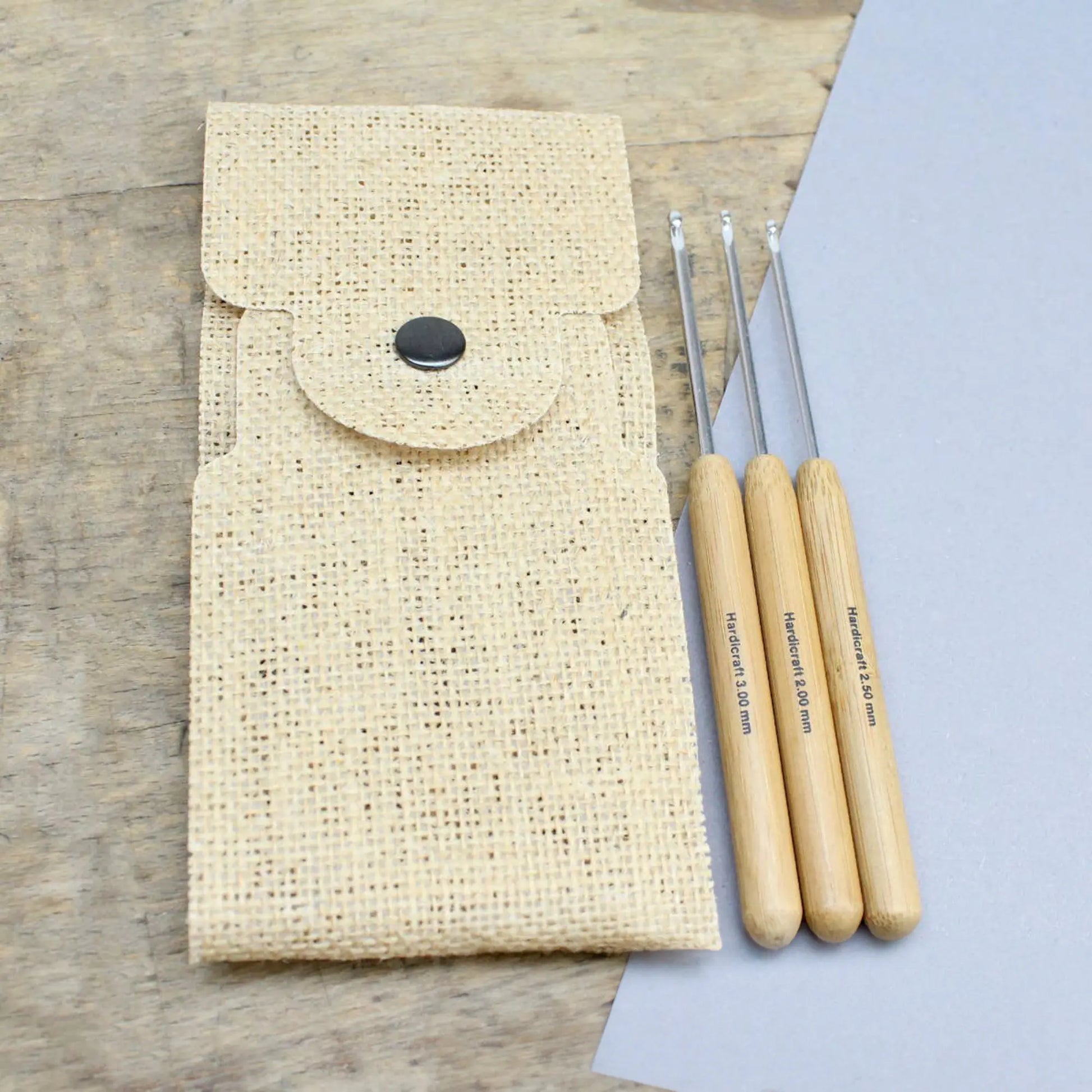 Three bamboo handle aluminum crochet hooks shown beside a natural burlap storage pouch on a tabletop