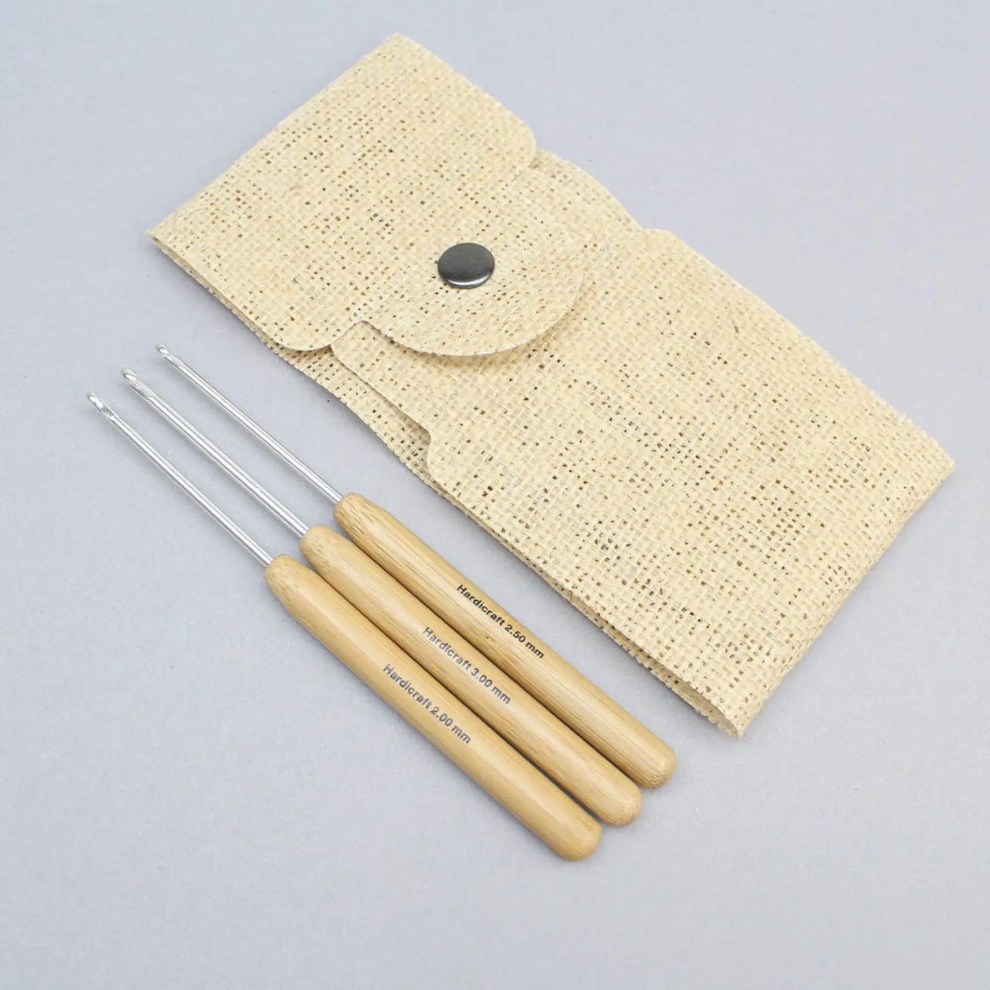 Bamboo handle aluminum crochet hook set with three fine-gauge hooks and burlap pouch on a gray background