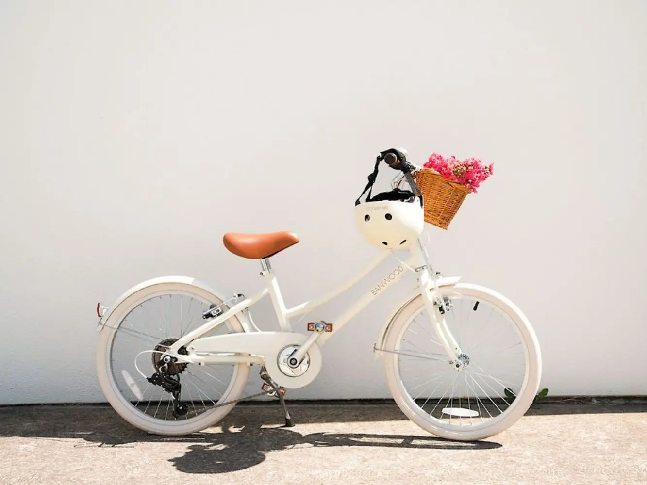 White cream bicycle with a basket of flowers against a plain background