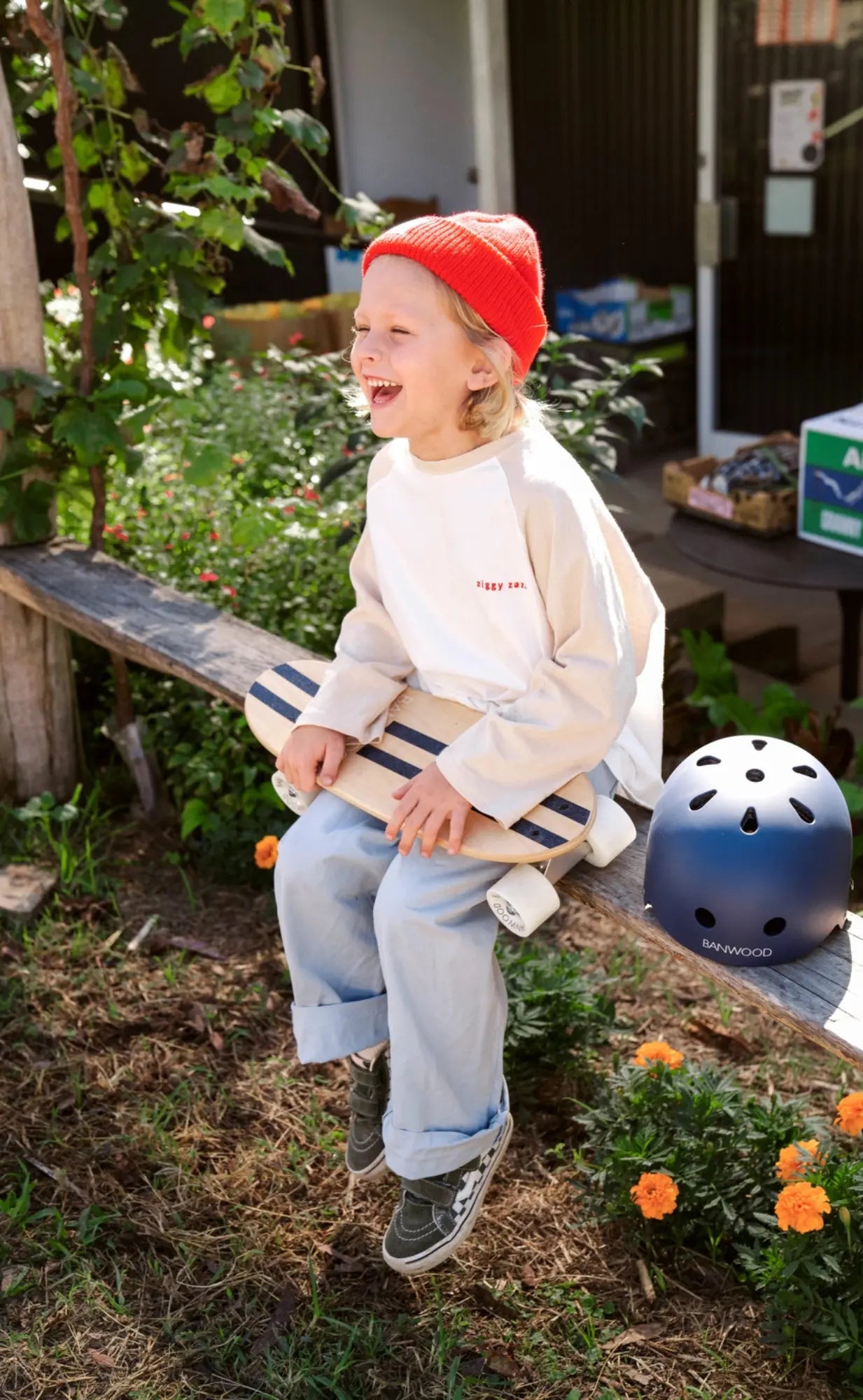 Child sitting on a wooden bench outdoors with a helmet nearby