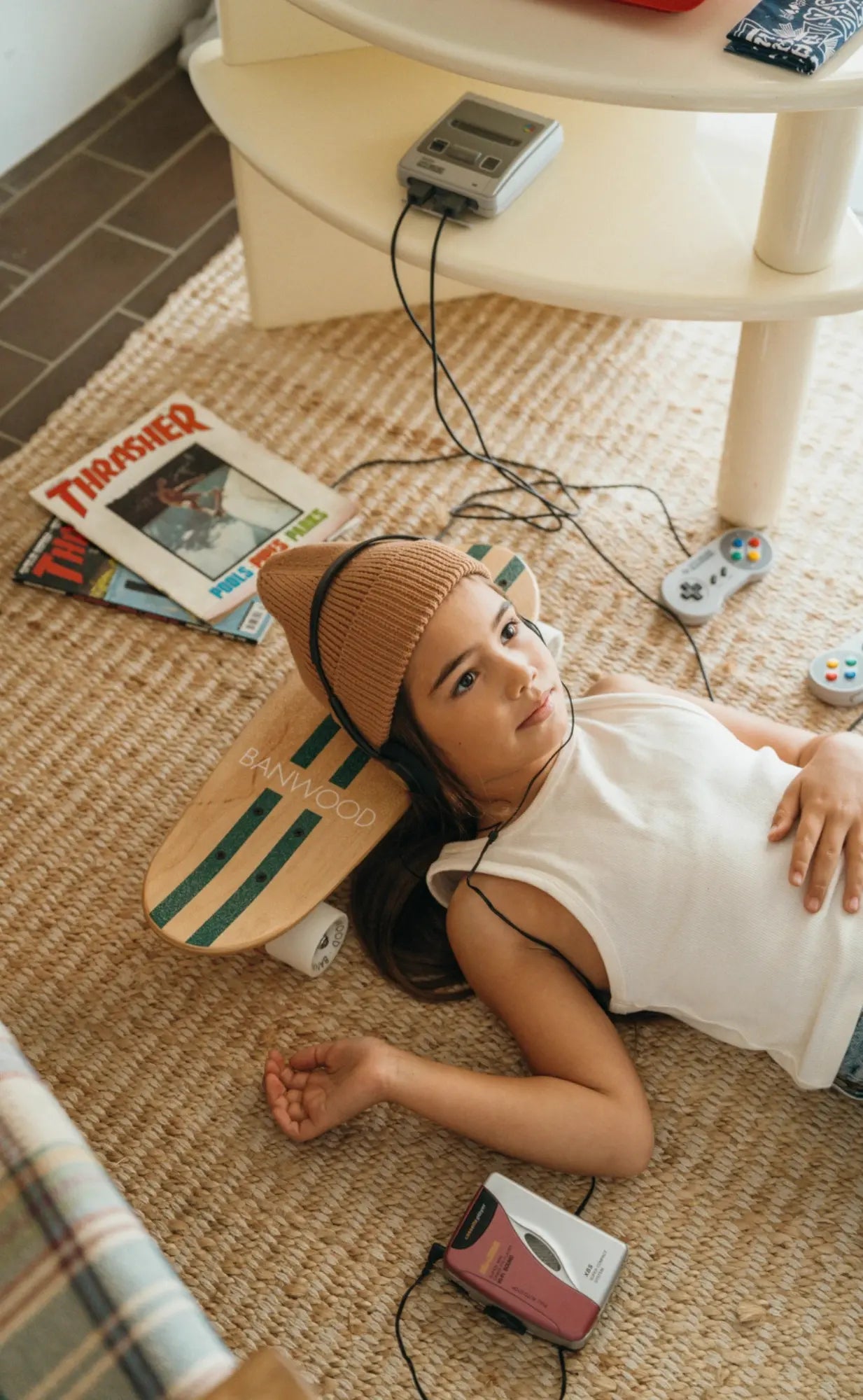 Person lying on a woven mat with a skateboard, cassette player, and magazines around them.