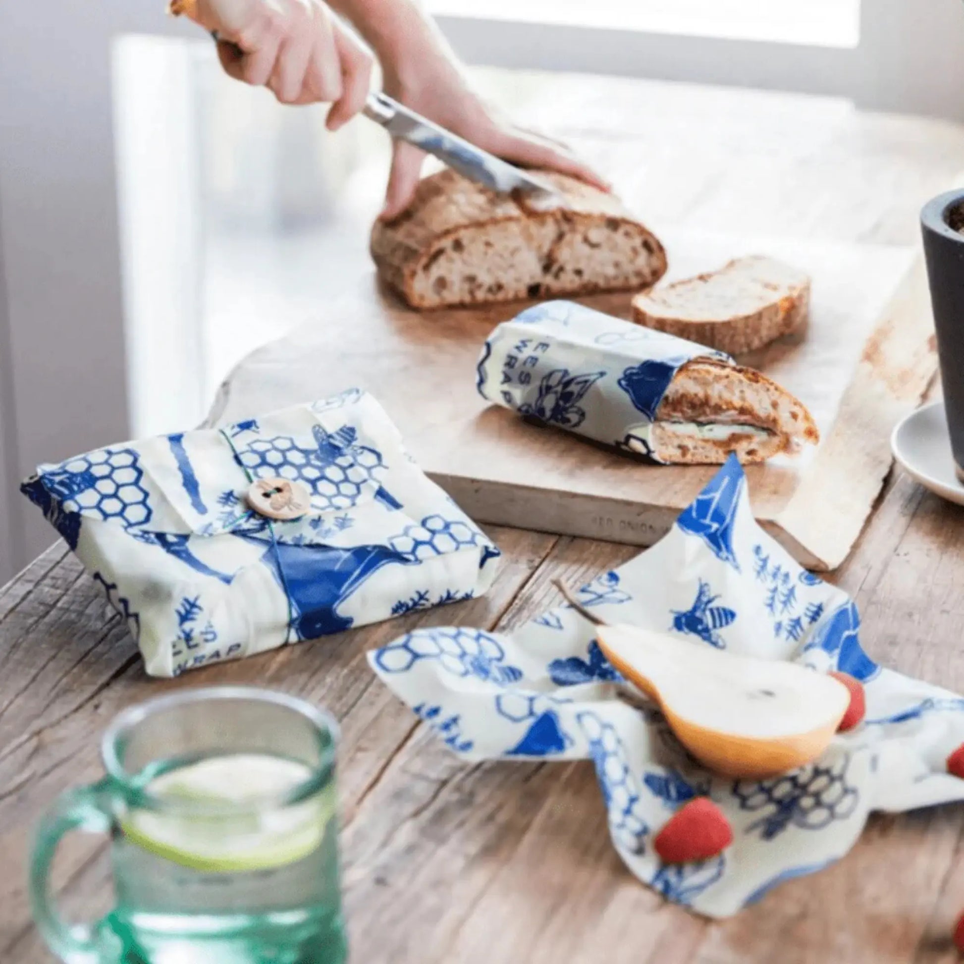 Reusuable beeswax food wraps on a wooden table with bread and fruit