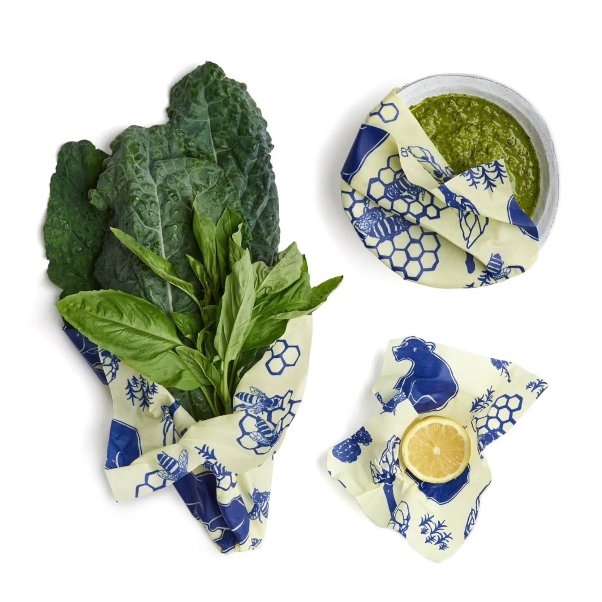 Reusable beeswax wraps with greens and a lemon on a white background
