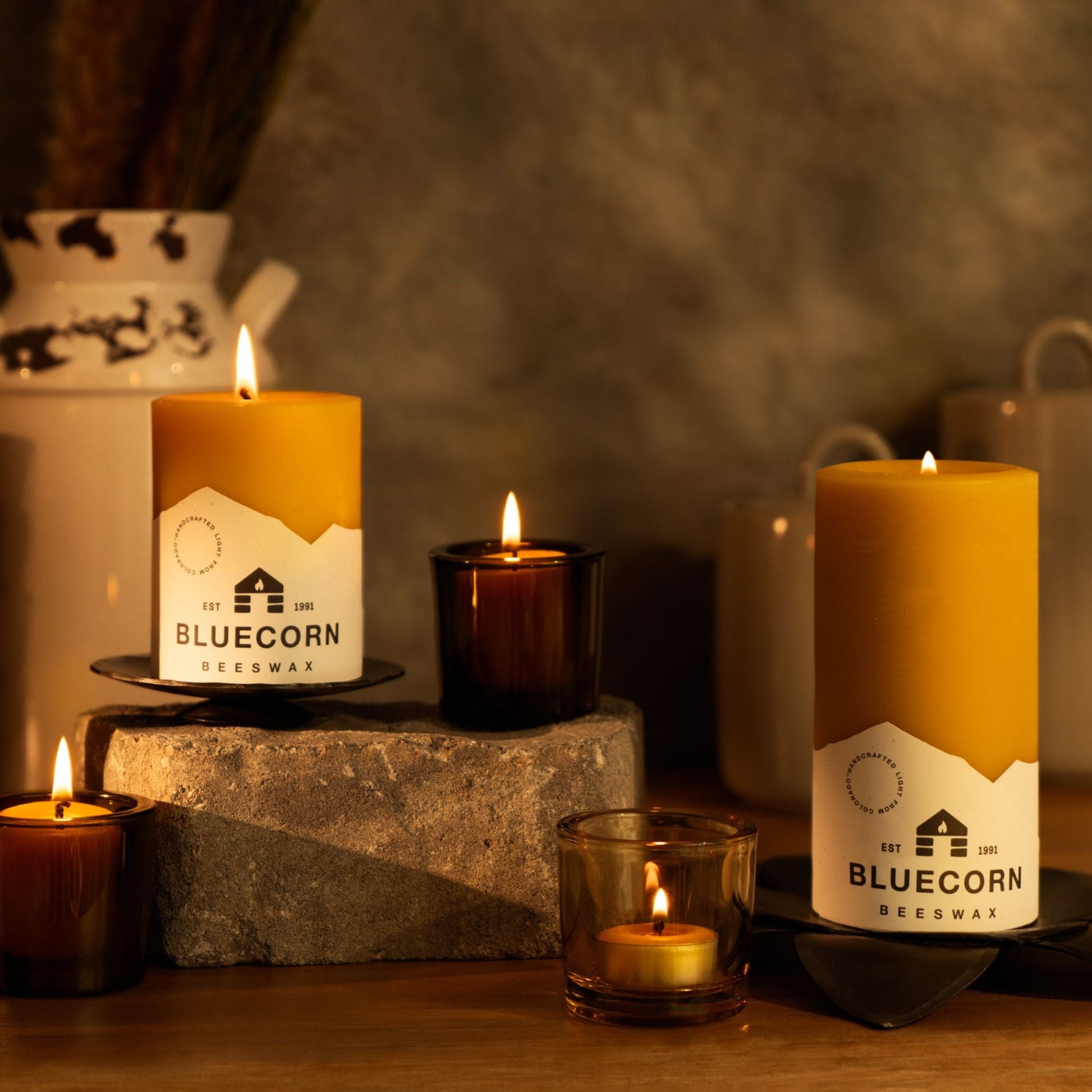 Candles with Bluecorn Beeswax branding on a wooden surface with a dark background