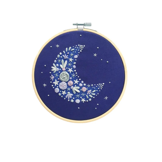 Embroidery hoop with a floral moon design on a blue background, surrounded by decorative stars and marbles.
