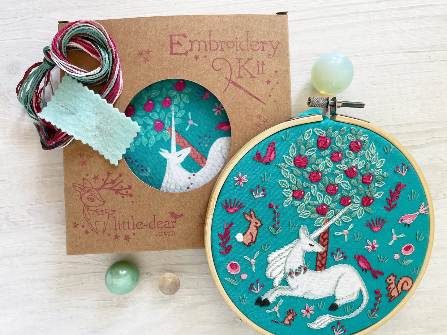 Embroidery kit with completed design featuring a unicorn and tree on a teal background with embroidery thread.
