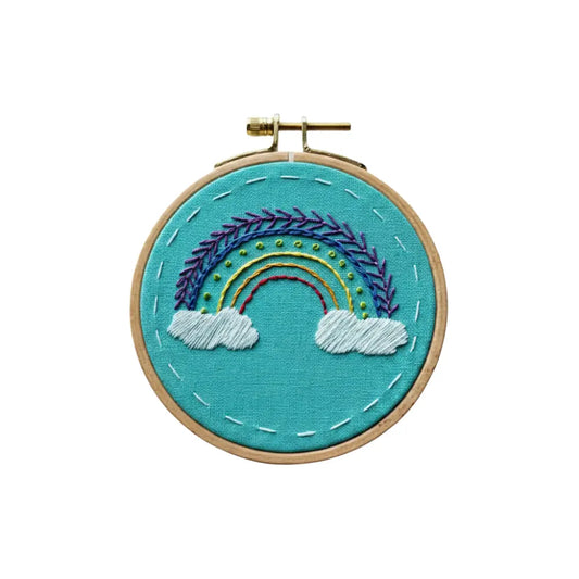 Embroidery hoop with a rainbow and cloud design on teal fabric.