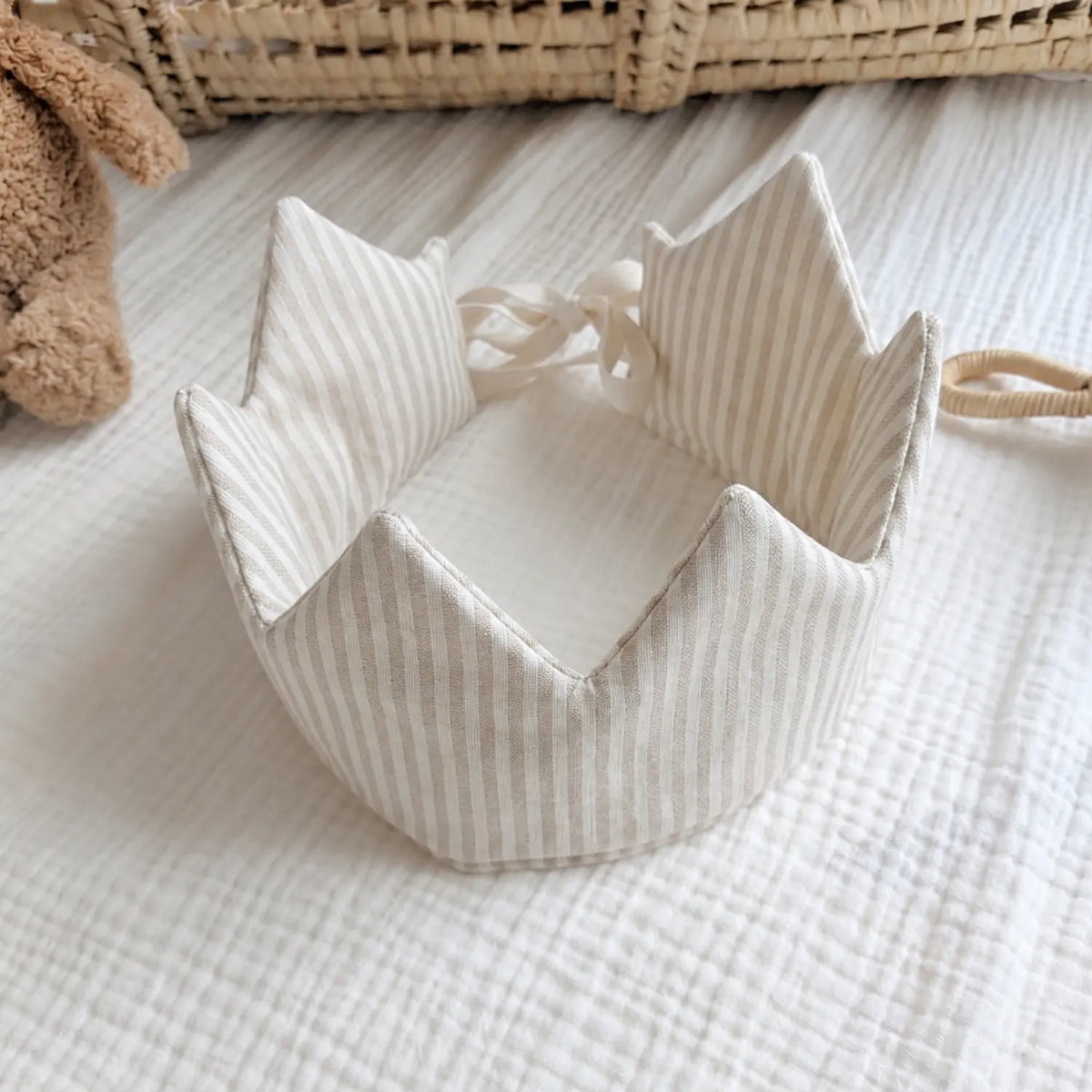 Beige striped linen children's crown shown open on a soft neutral nursery background