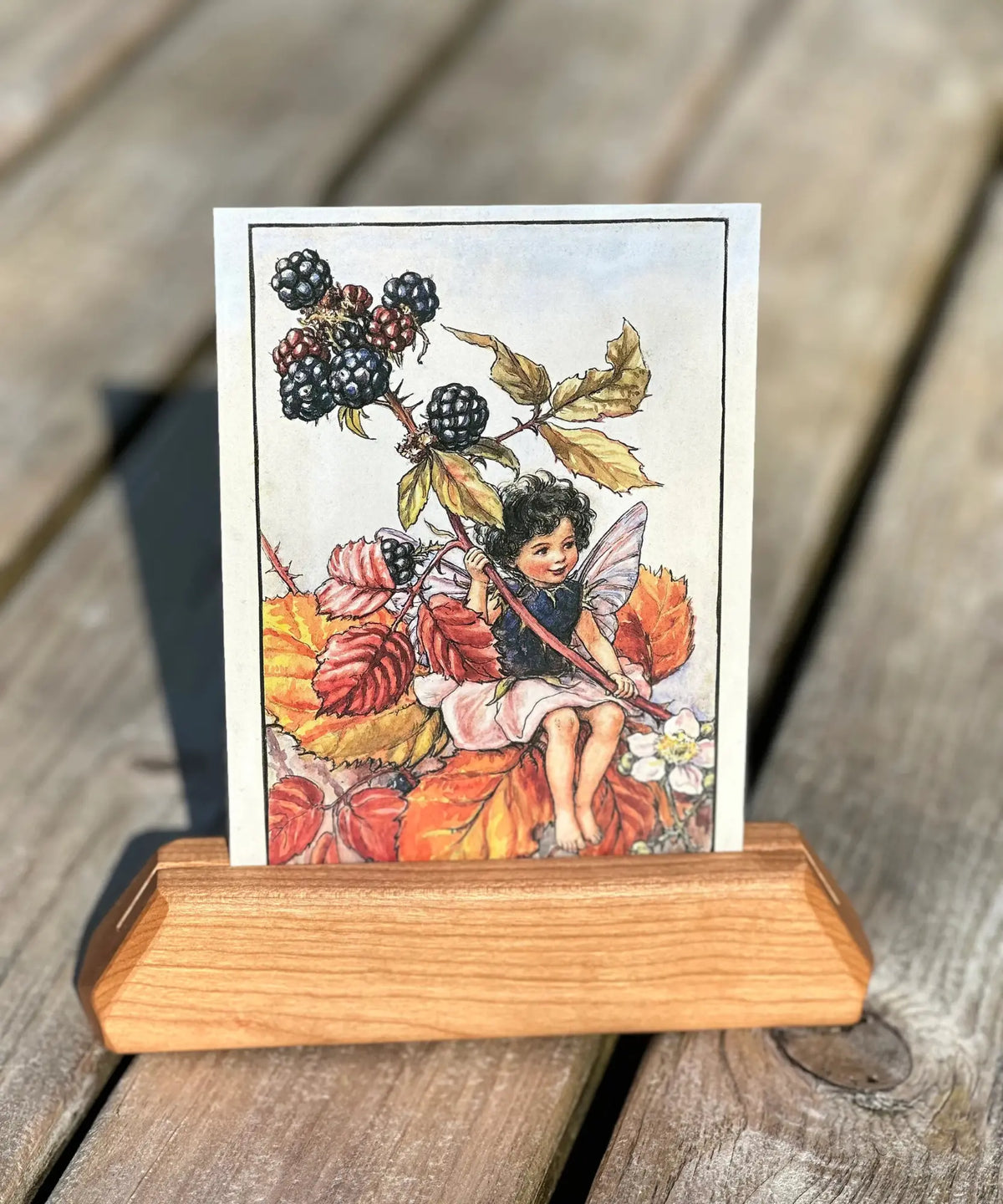 Blackberry fairy postcard by Cicely Mary Barker in a wooden stand on a rustic wood table