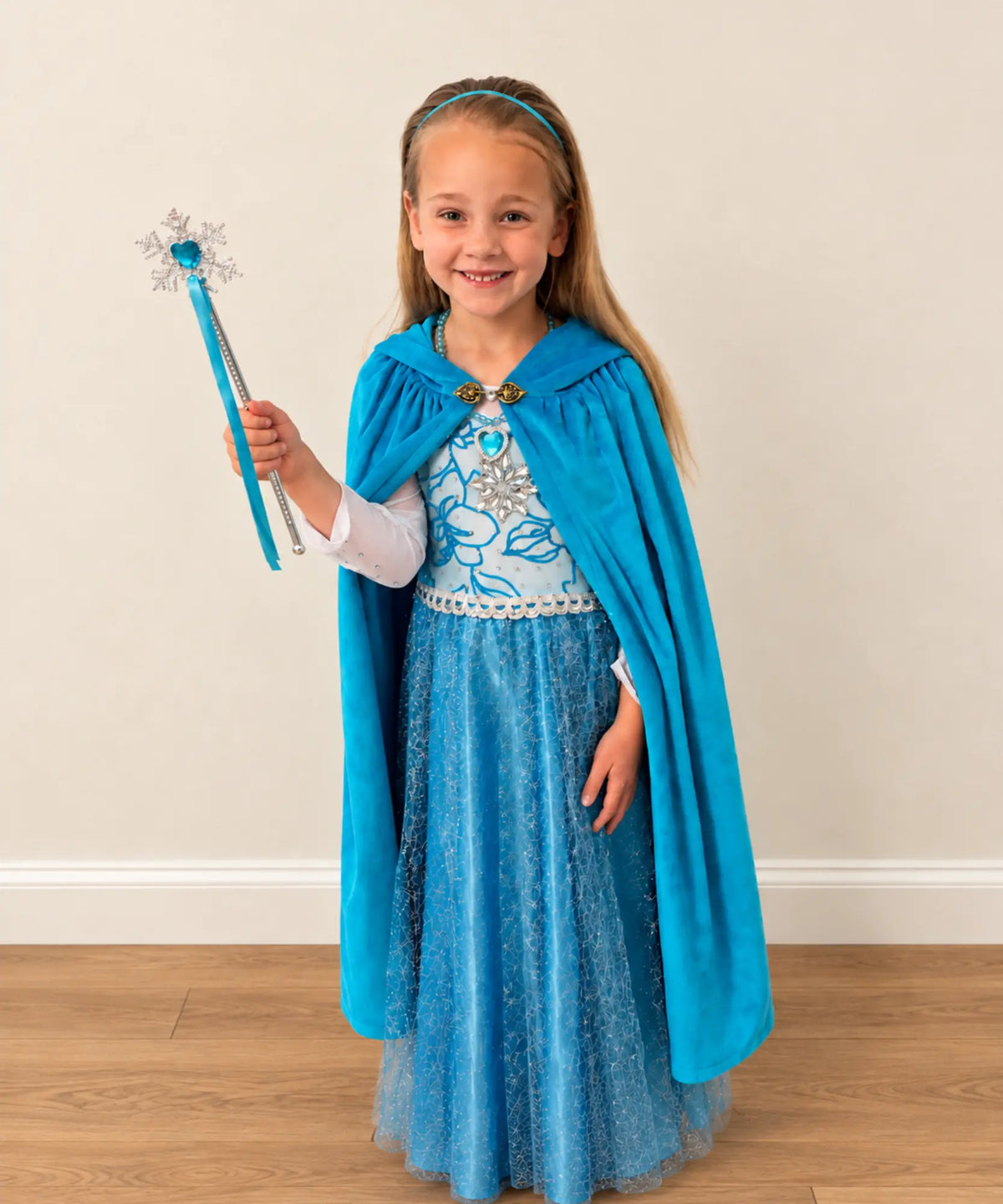 A young girl stands indoors wearing an Elsa-inspired costume with a bright blue cape