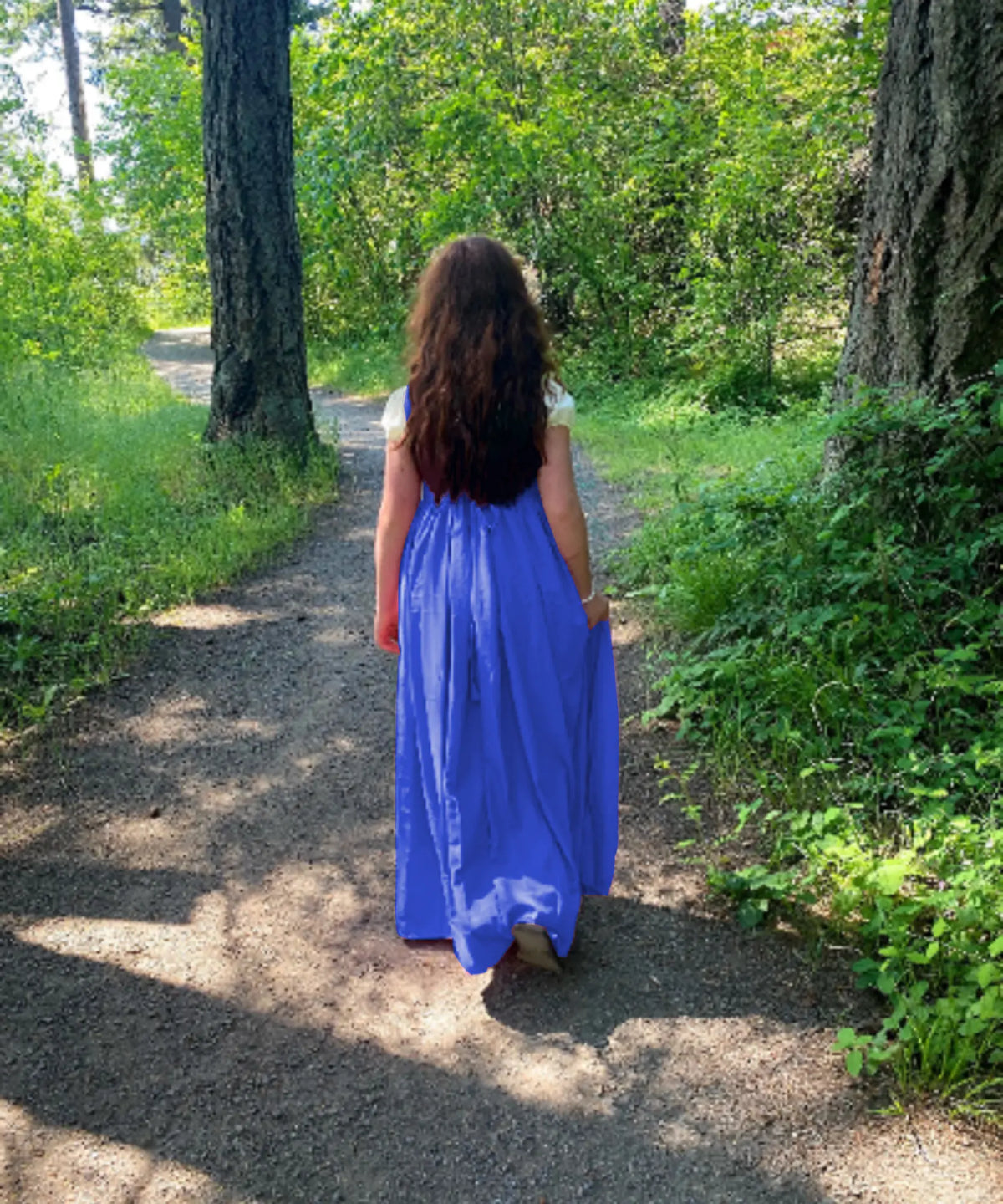 Back view of a child wearing the blue storybook princess dress while walking along a woodland path.
