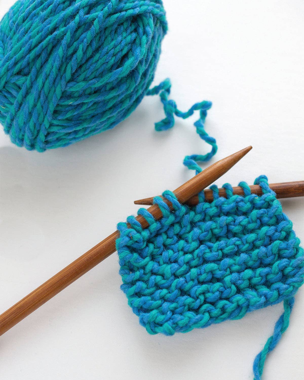 Blue and teal wool yarn knit in garter stitch on wooden needles from the Friendly Loom beginner scarf kit