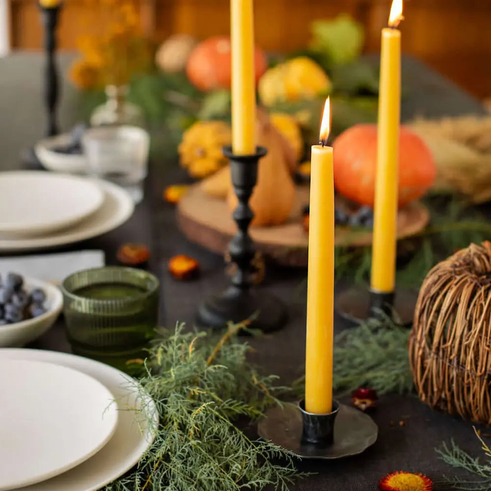 Decorative table setting with candles, plates, and pumpkins in a warm indoor setting.