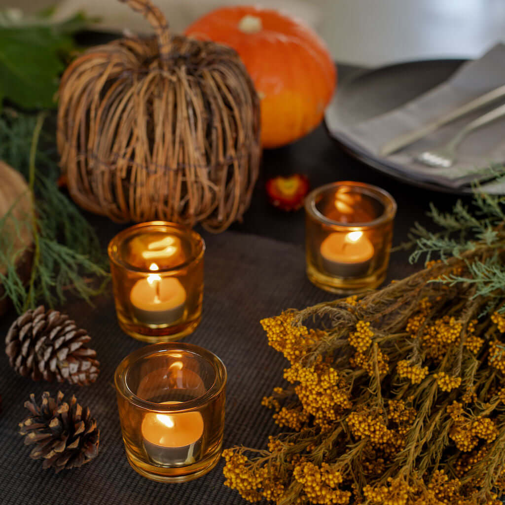 Autumn-themed table setting with candles, pumpkins, and decorative elements on a dark surface.