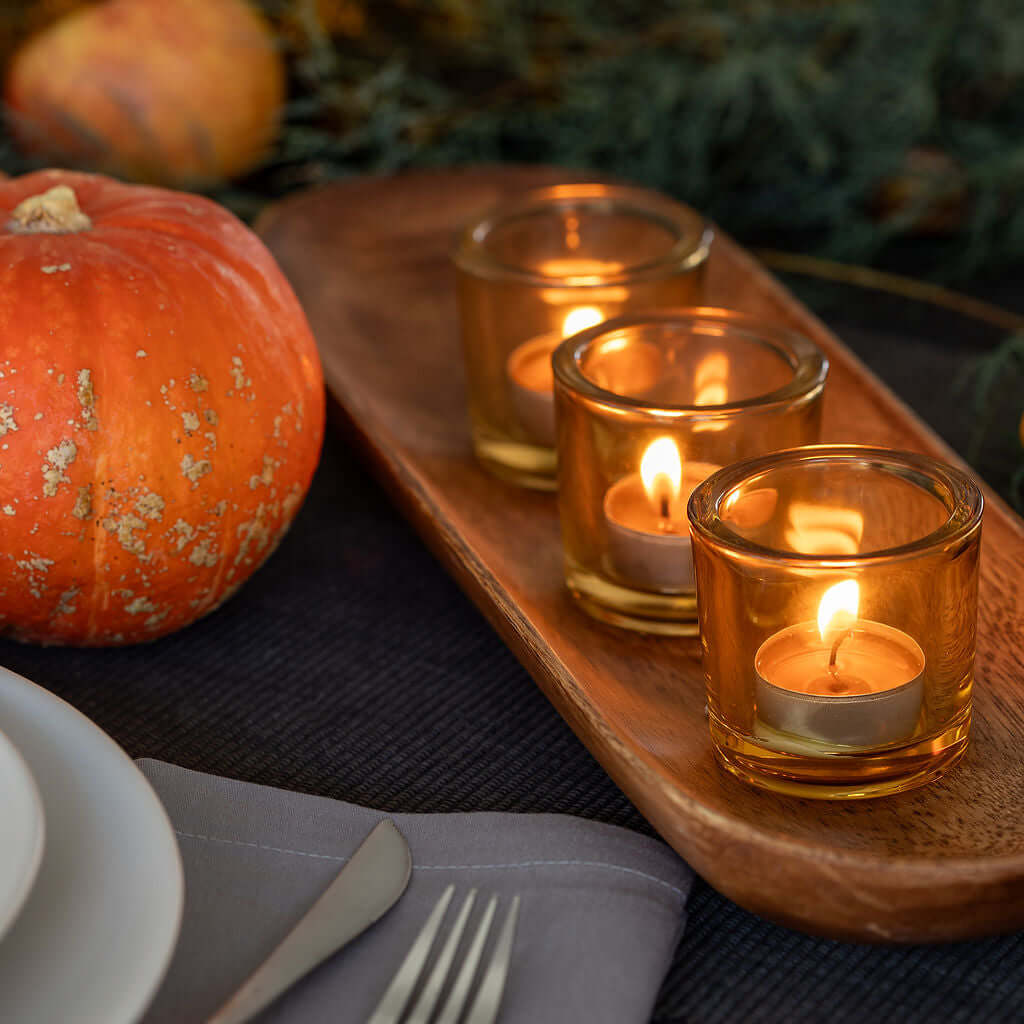 Candlelit setting with pumpkins and a wooden tray on a table.