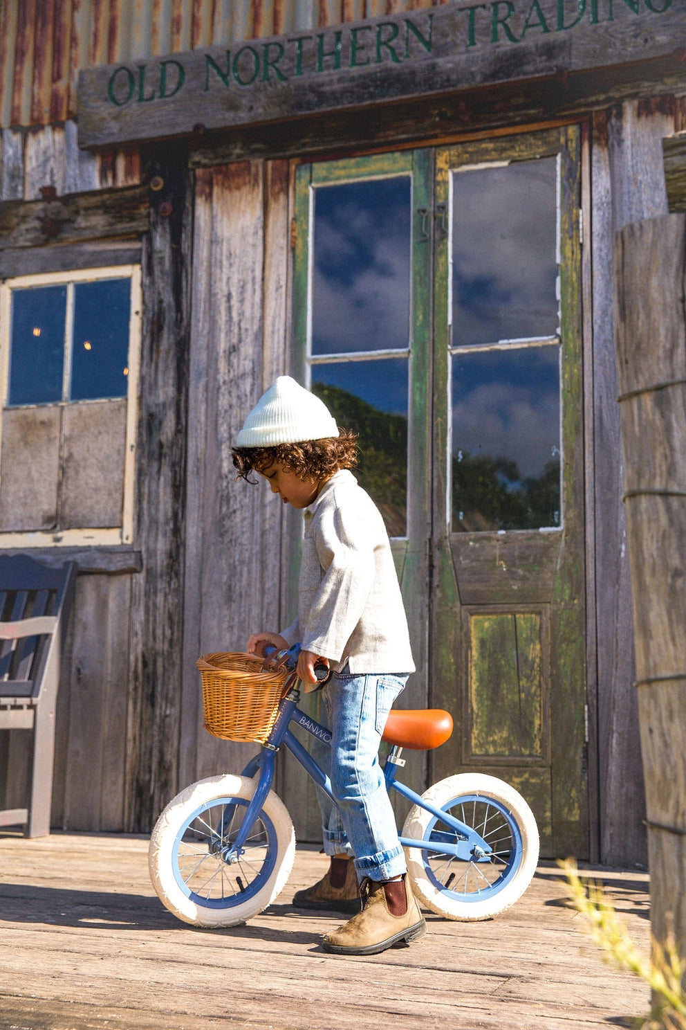 Child with a blue bicycle in front of an old wooden building