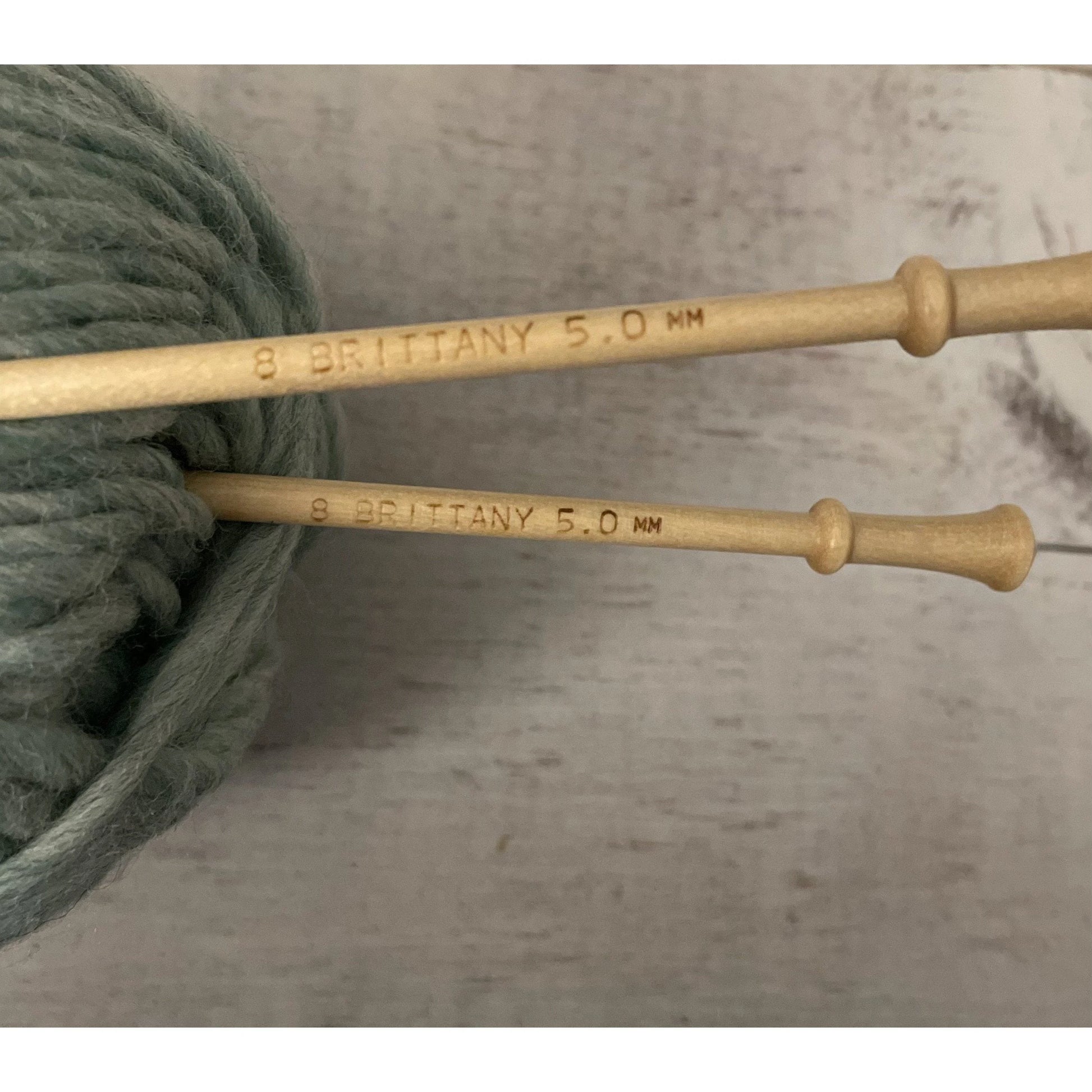 Close-up of Brittany birch wood knitting needles showing size markings beside green wool yarn
