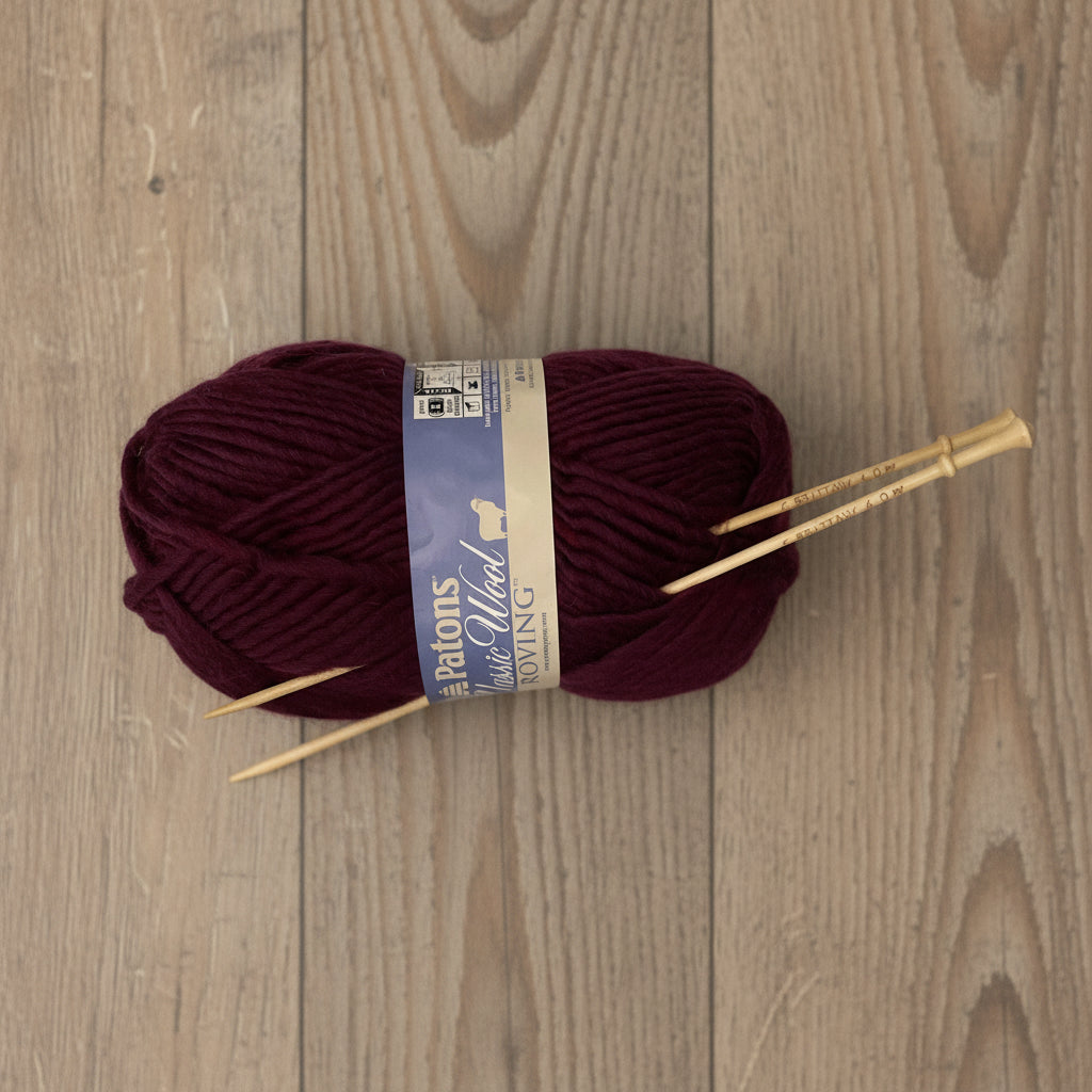 Brittany birch wood knitting needles with burgundy wool yarn on a natural wood surface
