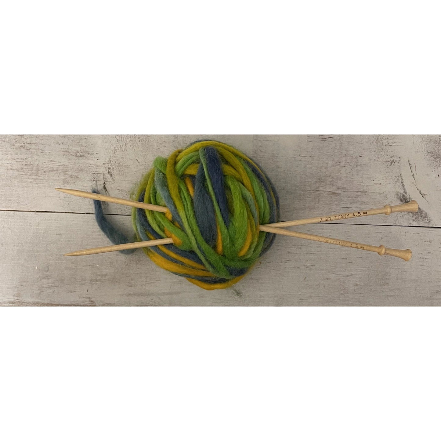 Brittany birch wood knitting needles tucked into a ball of green variegated wool yarn