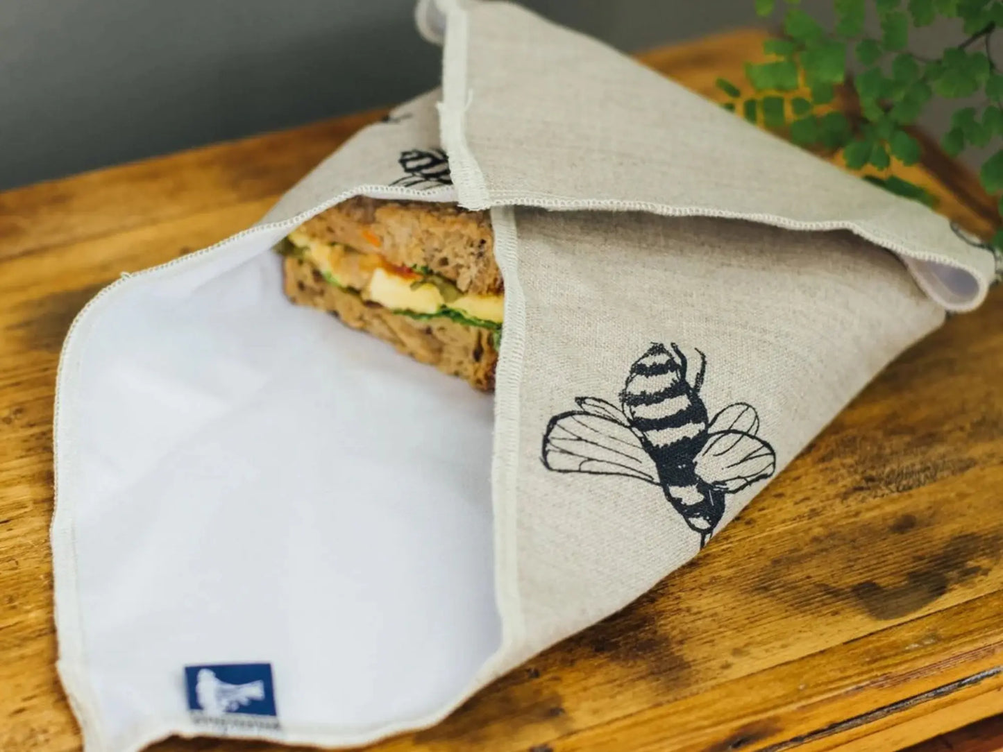 Linen lined sandwich wrap with a bee design on a wooden surface with a sandwich inside
