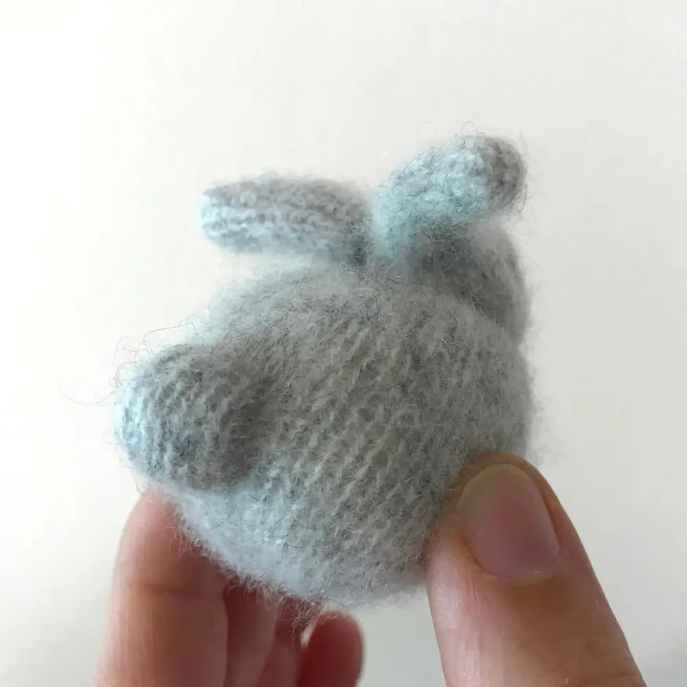 Small hand sewn cashmere bunny resembling a cat held between fingers on a white background