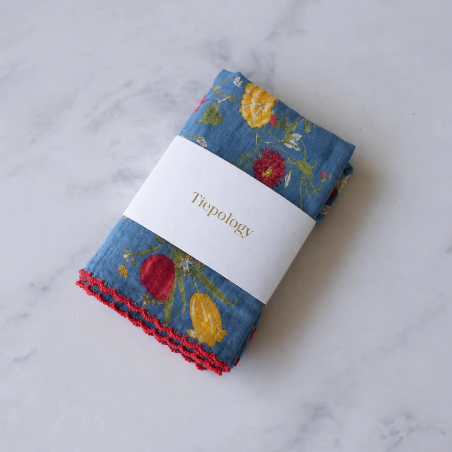 Folded Cecilia Floral cotton blend square scarf by Tiepology in a denim blue floral print with red edging