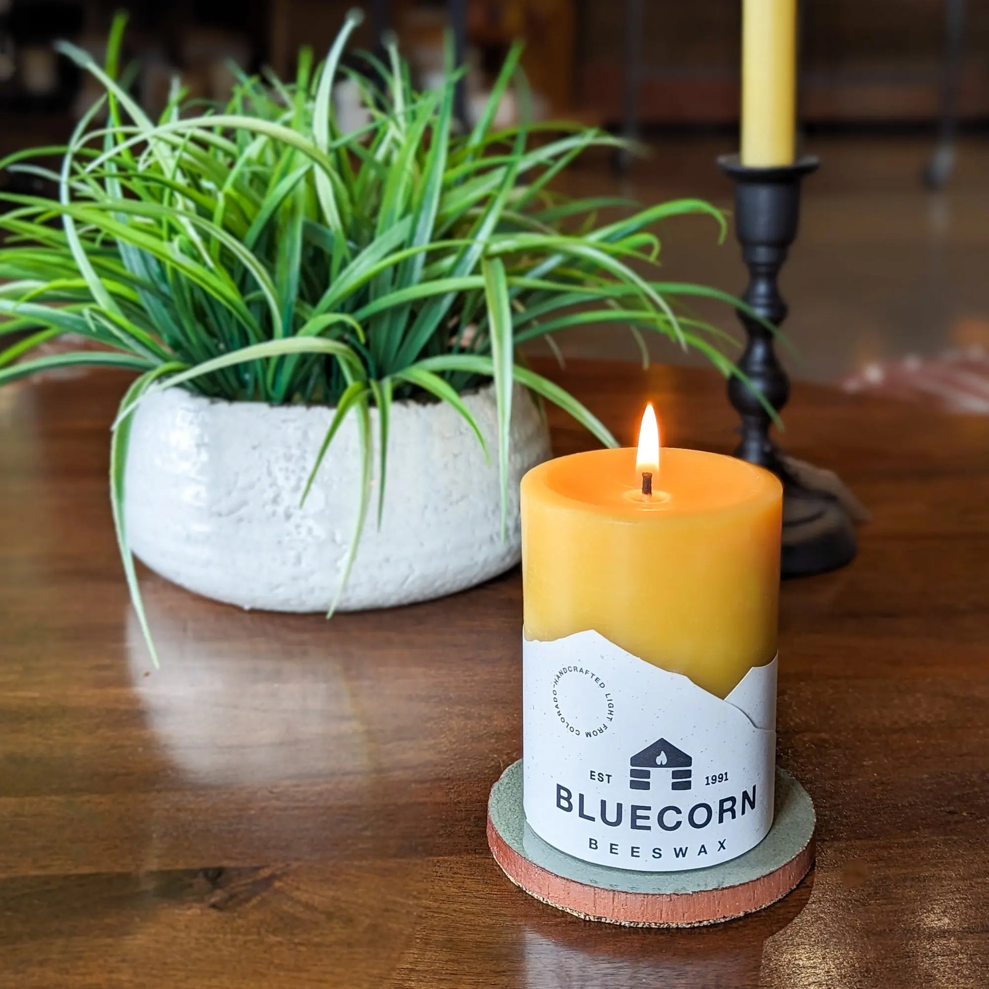 Glazed ceramic pillar candle base holding a beeswax pillar candle on a wooden table